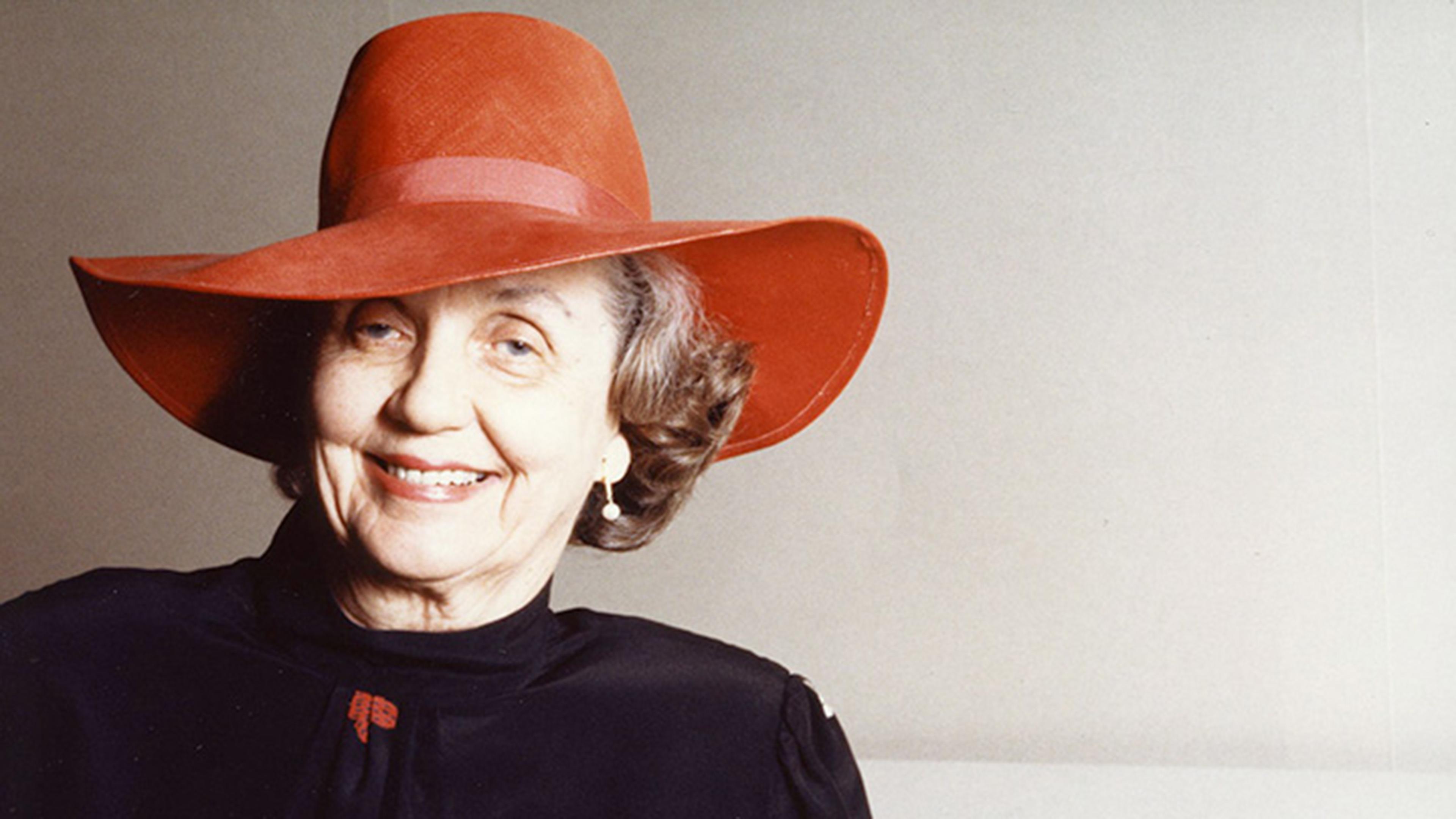 Mary Griggs Burke wearing a red hat and a black jacket with red, white, and black butterfly motifs