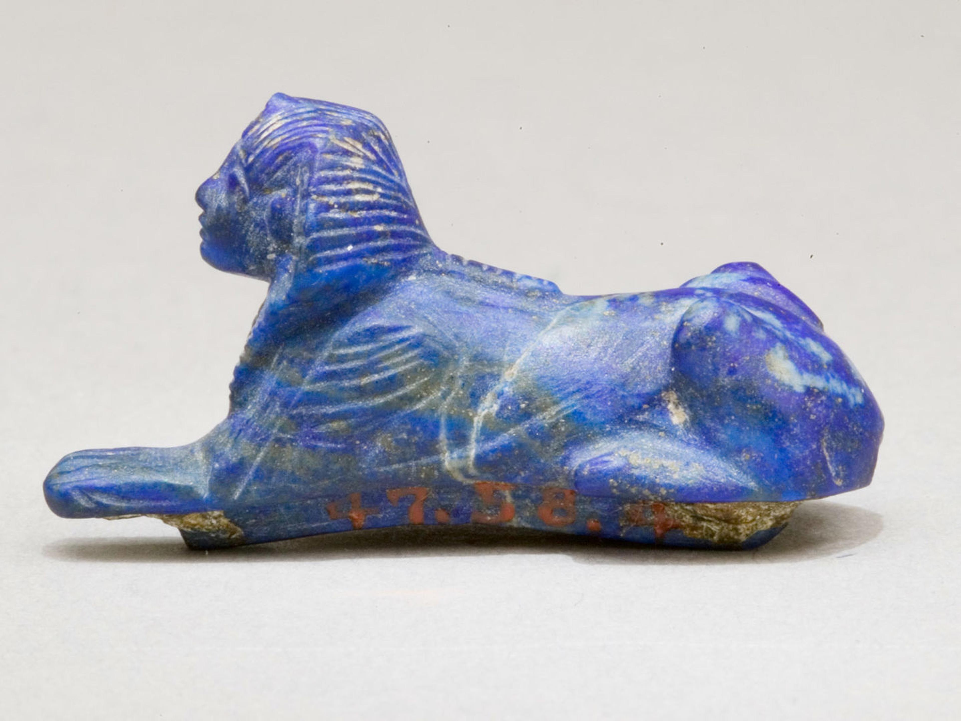 A small, carved lapis lazuli sphinx sculpture with intricate detailing, depicting a lion's body and human-like head.