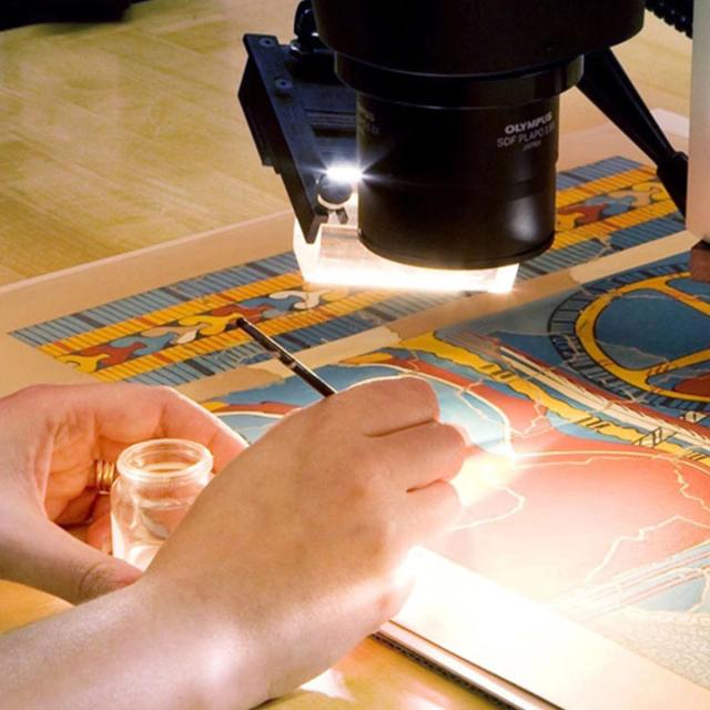 A woman looking through a telescope, examining a colorful work of art on paper