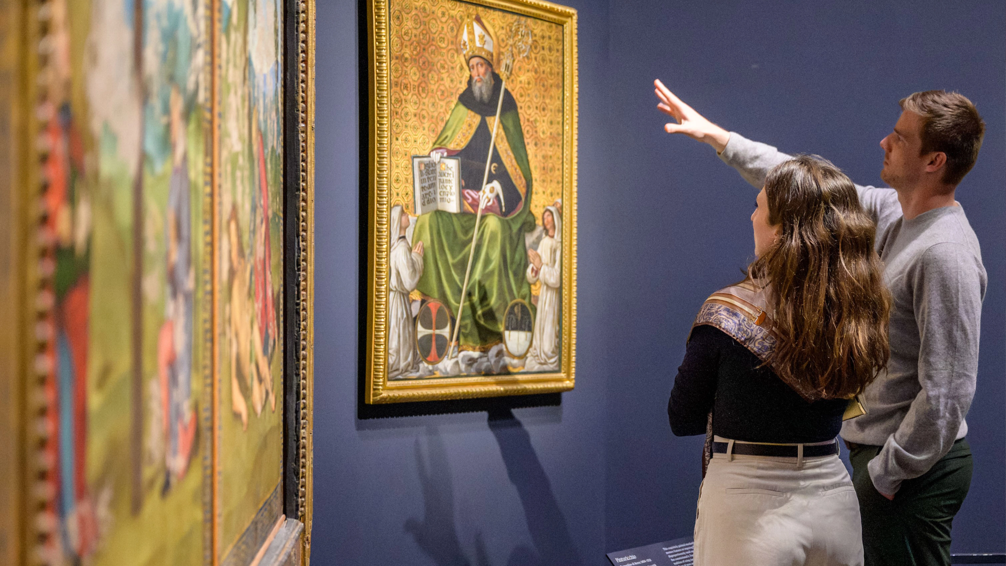 Two people point at a painting. 