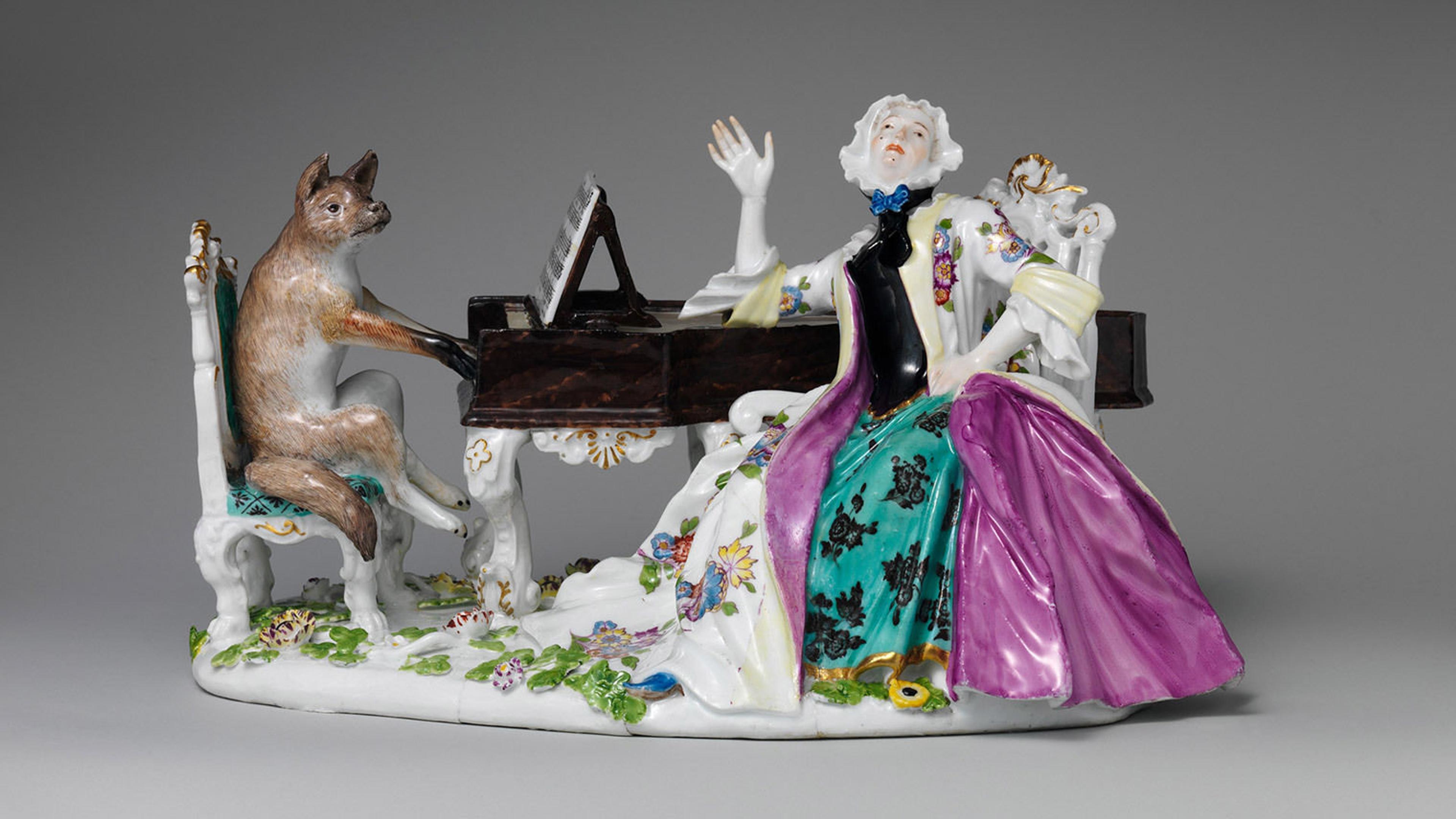 Sculpture of a fox sitting on a bench playing the piano while a regally dressed woman looks upwards