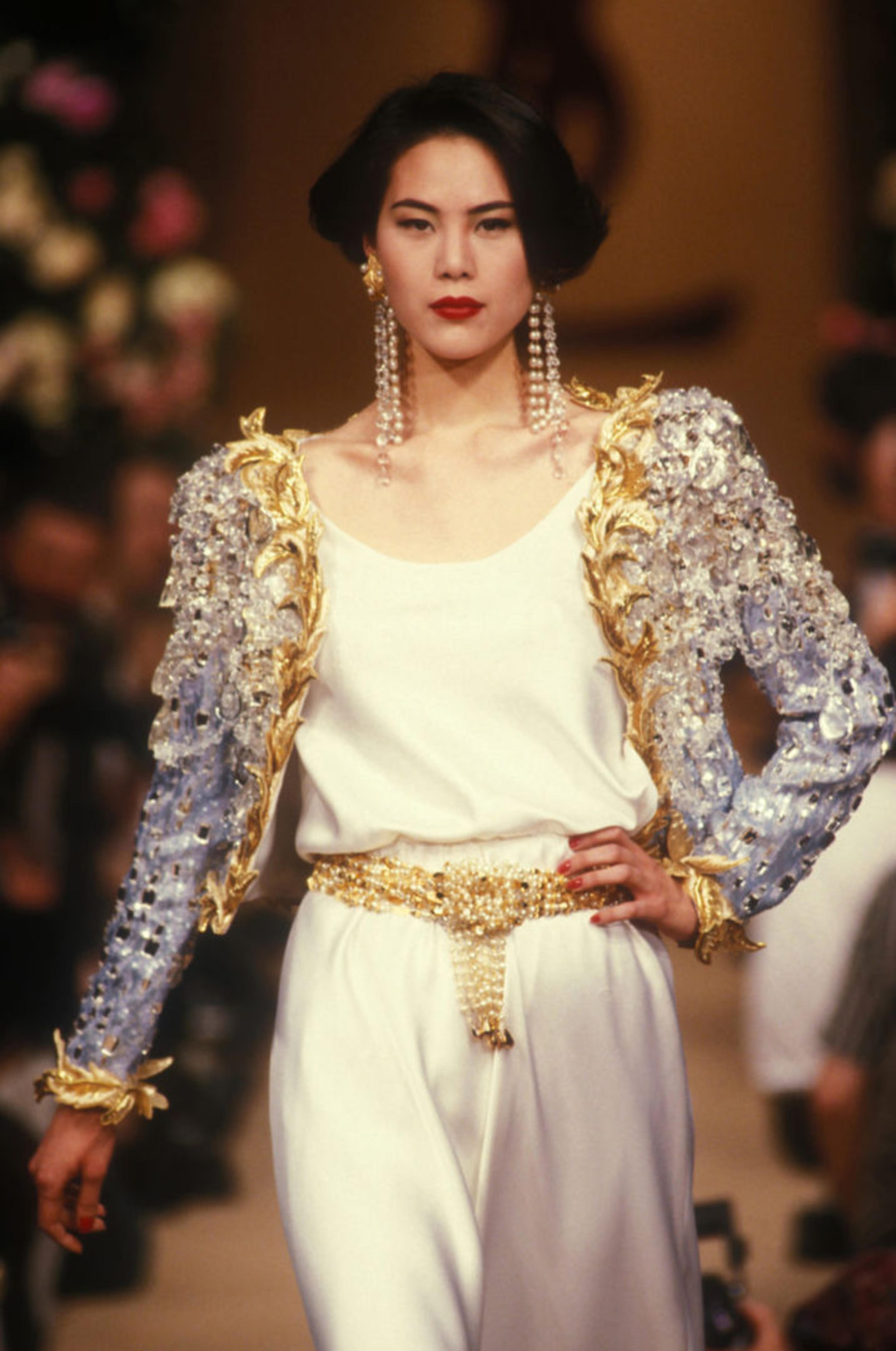 Model wearing a white silky outfit and a silver and gold embroidered jacket designed by Yves Saint Laurent
