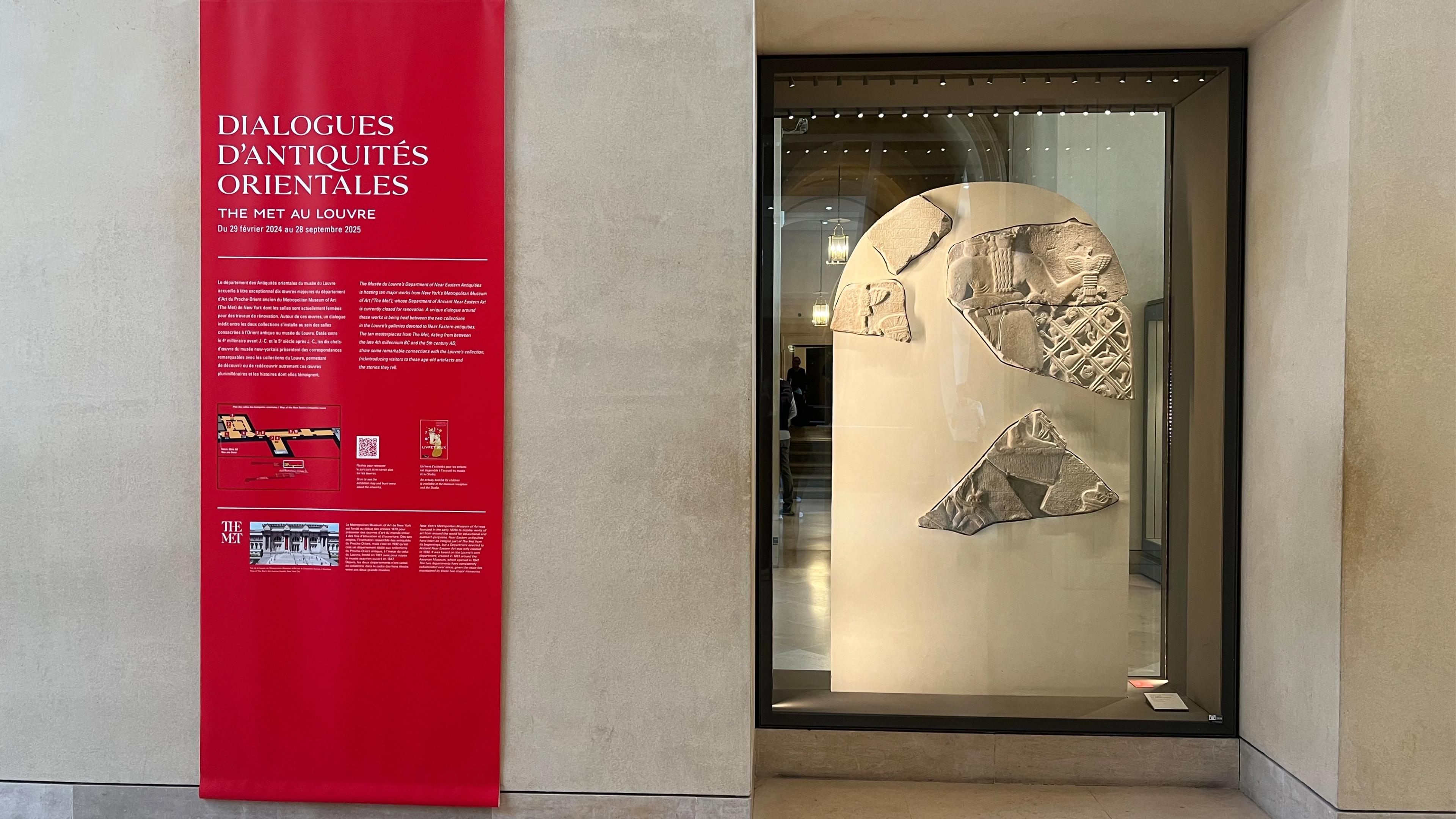 Red banner at the entrance to exhibition galleries at The Louvre hanging next to a larger ivory stone
