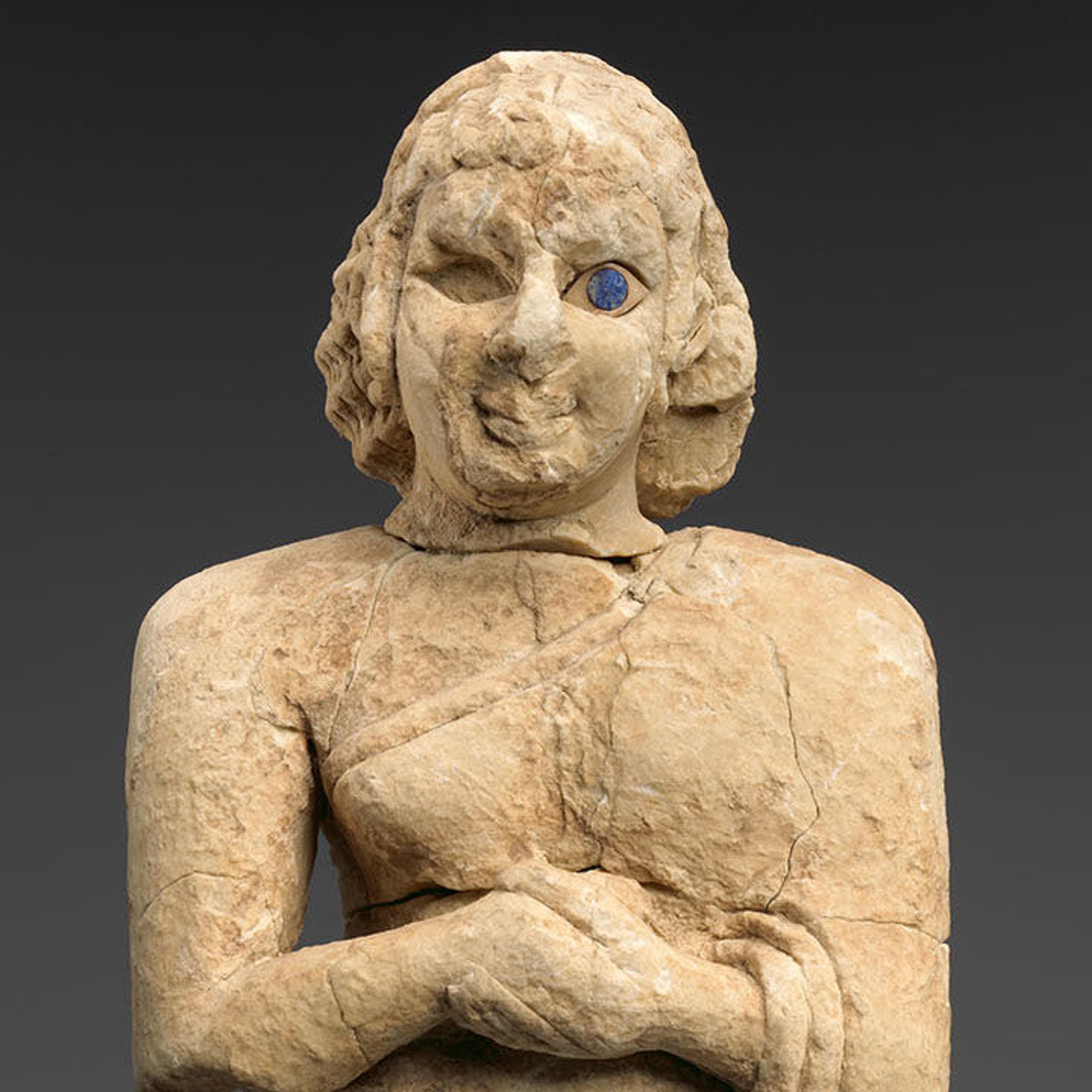 A limestone sculpture of a woman standing with hands clasped in prayer. Inlaid with shell and lapis lazuli for details.
