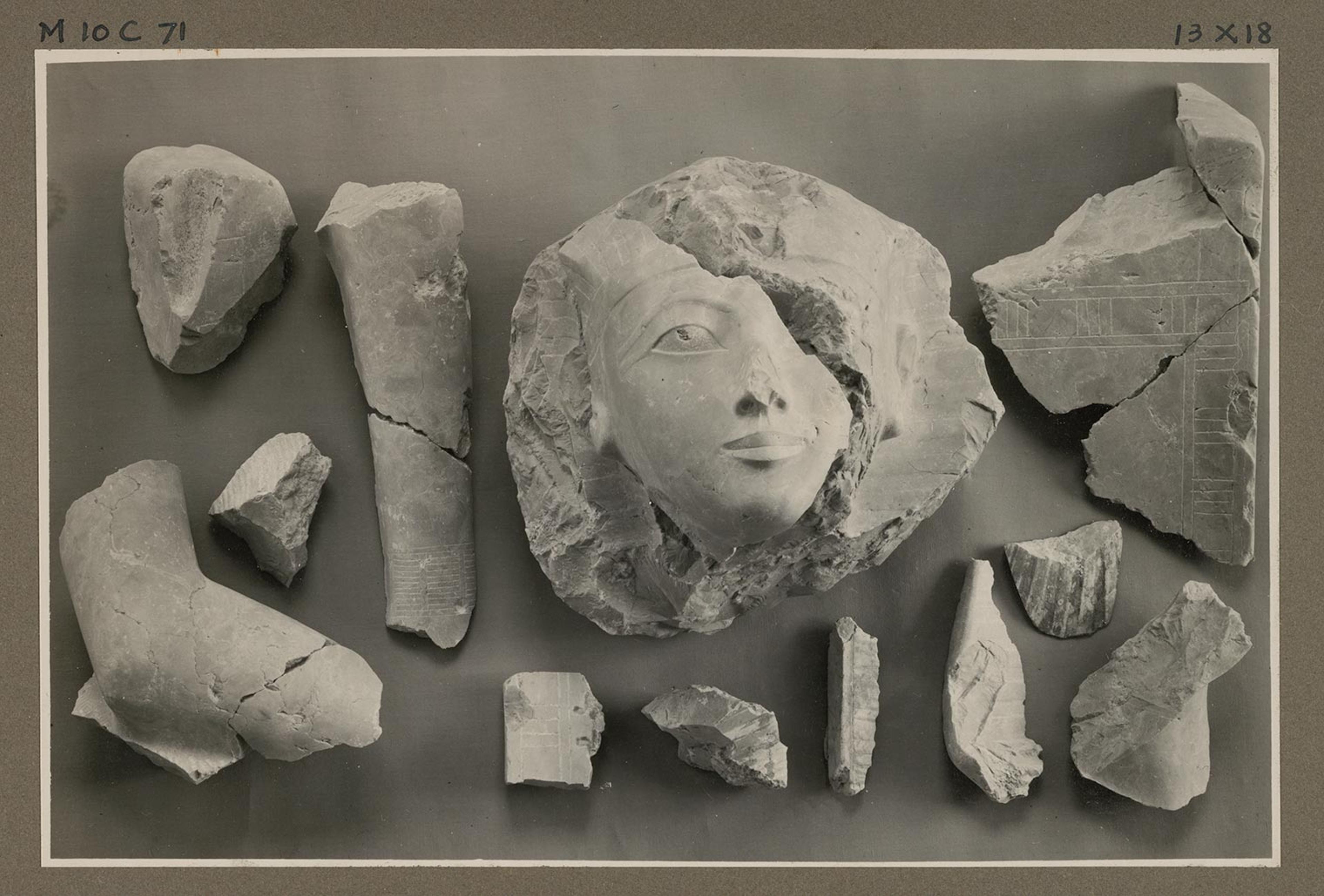 A black and white photograph of fragments of an ancient Egyptian statue displayed on a table.
