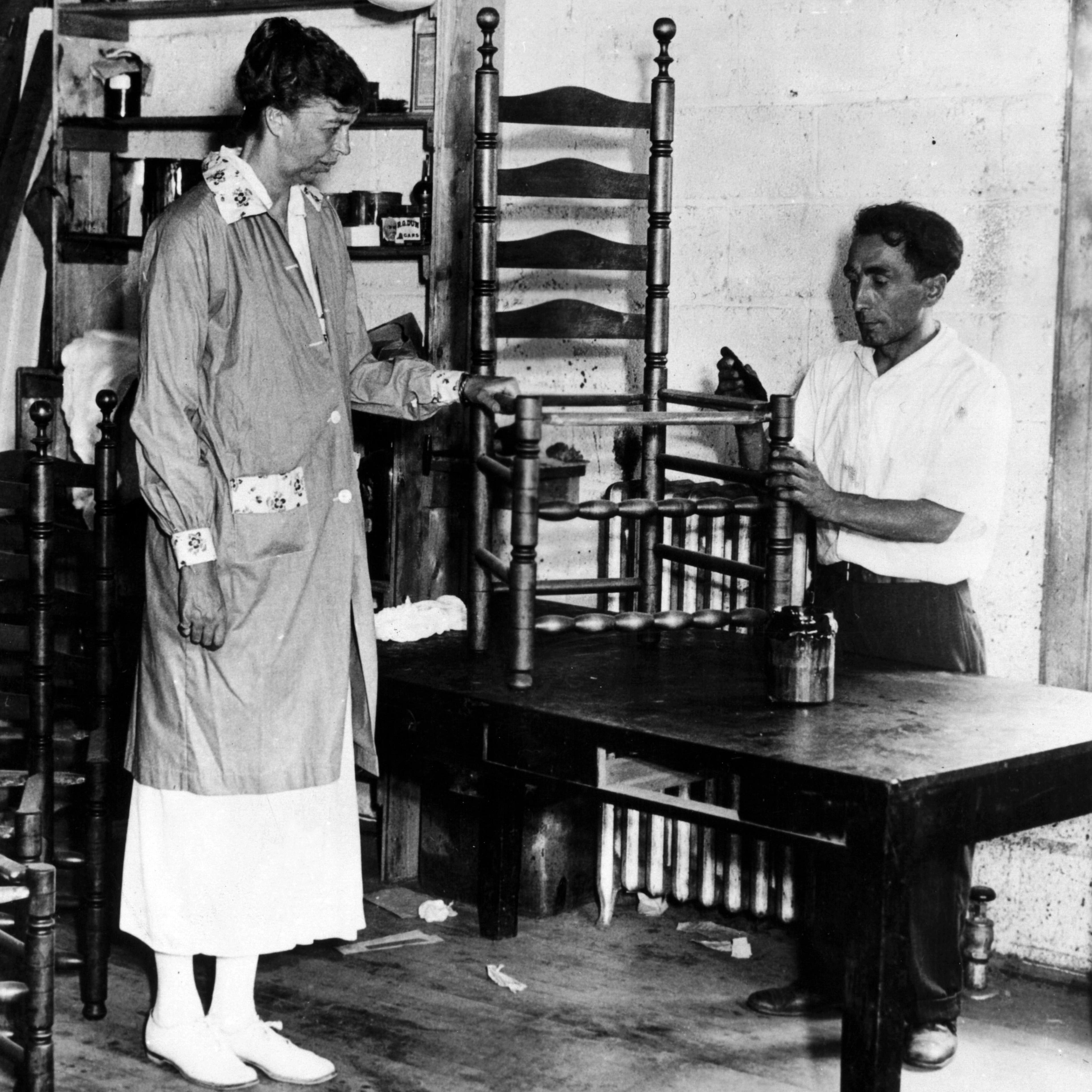 Black and white photo of a man and woman fixing a wooden chair
