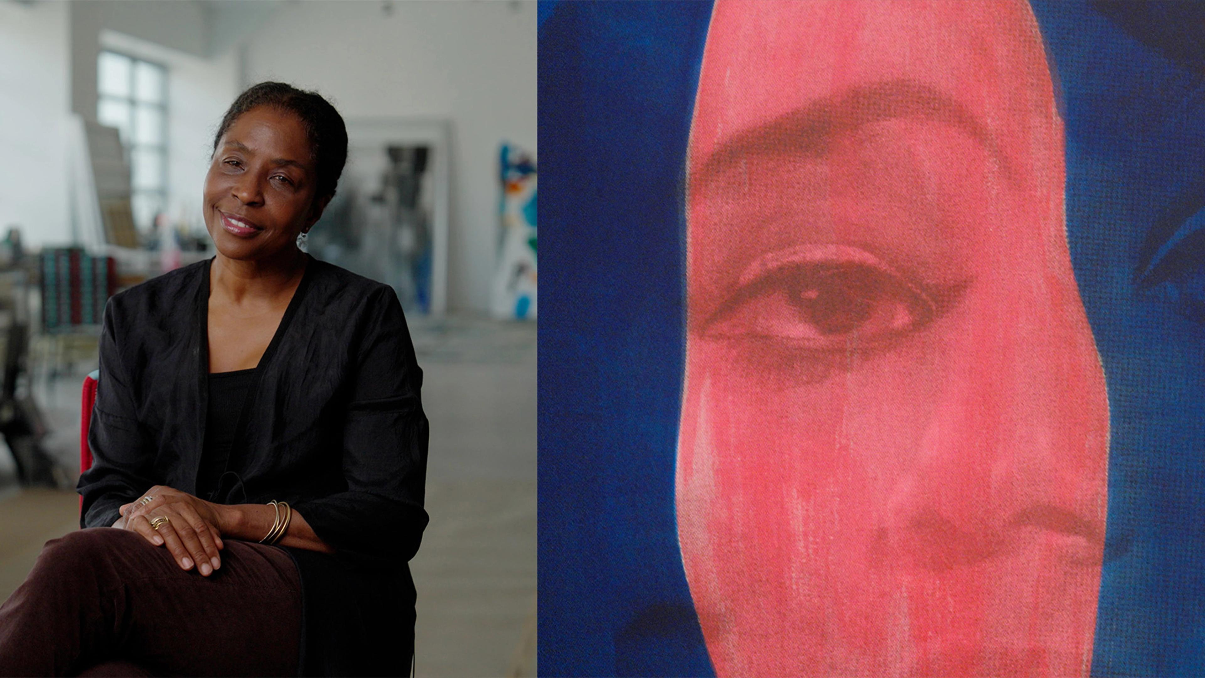 A woman in a black outfit sits in a bright studio, smiling softly. Beside her, a vibrant portrait shows a woman's face in red and blue tones.
