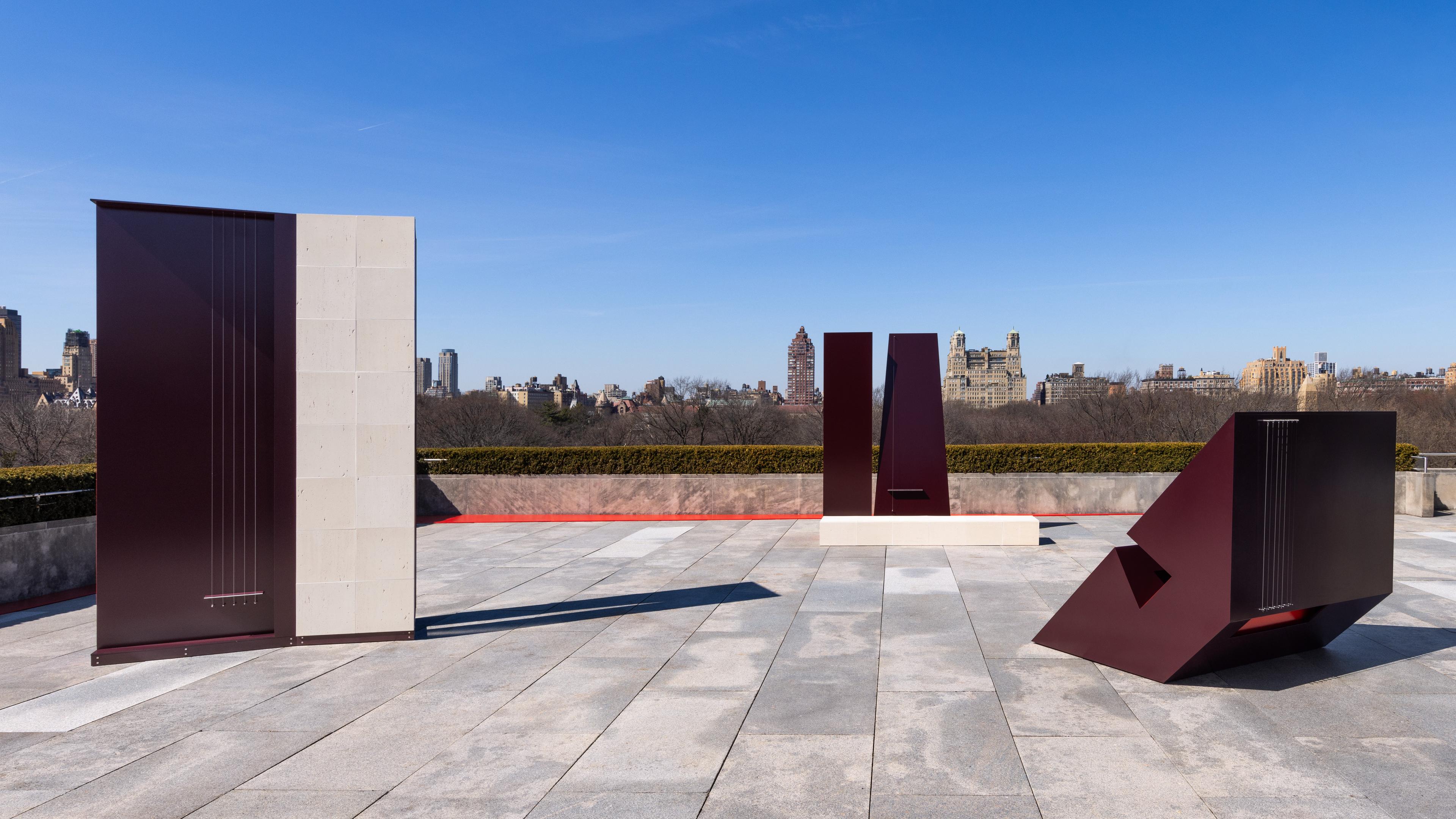 Three geometric sculptures with strings sitting on a roof overlooking a city skyline