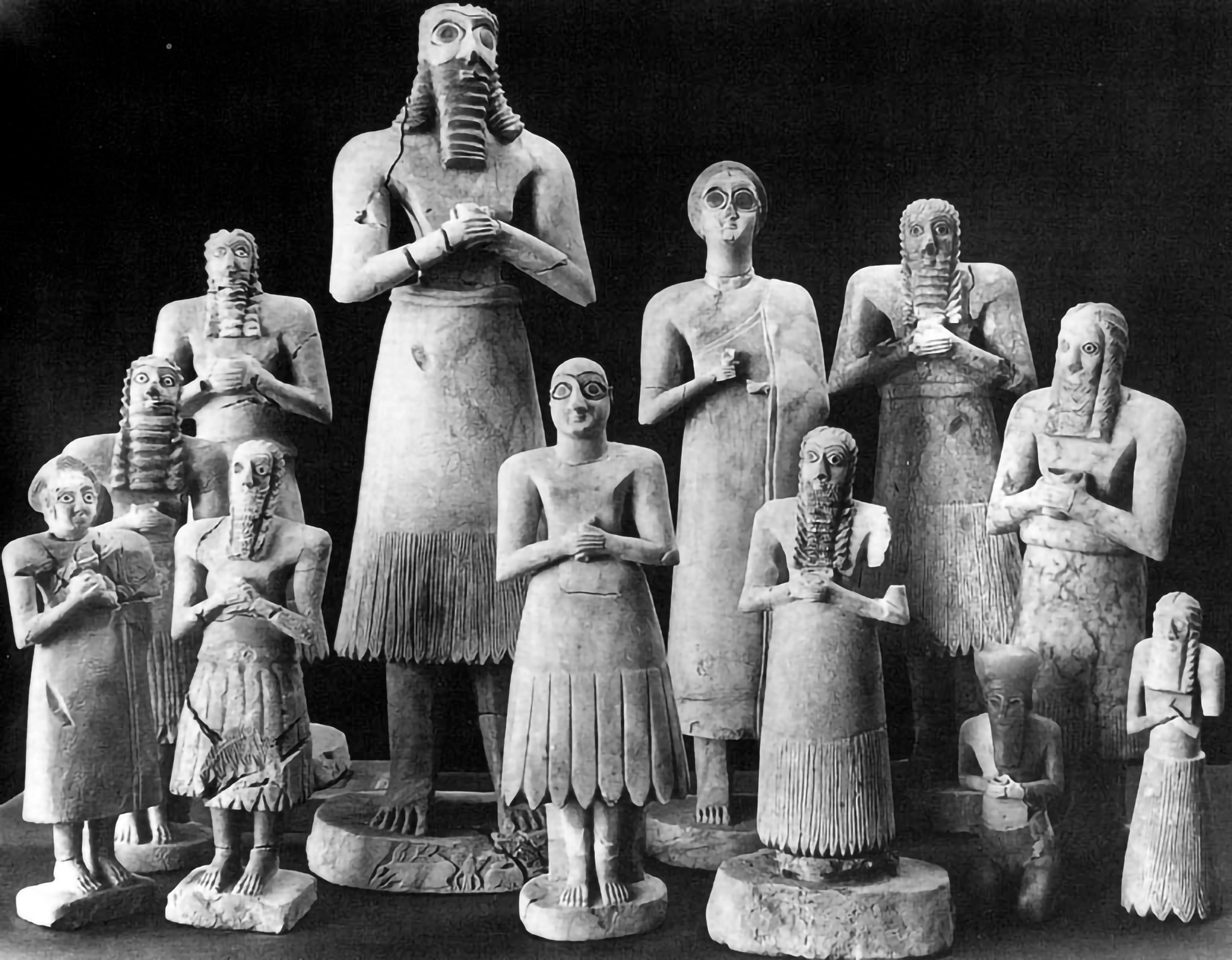 Black-and-white photo of twelve varyingly-sized stone figures, all with their hands clasped in a devotional pose.