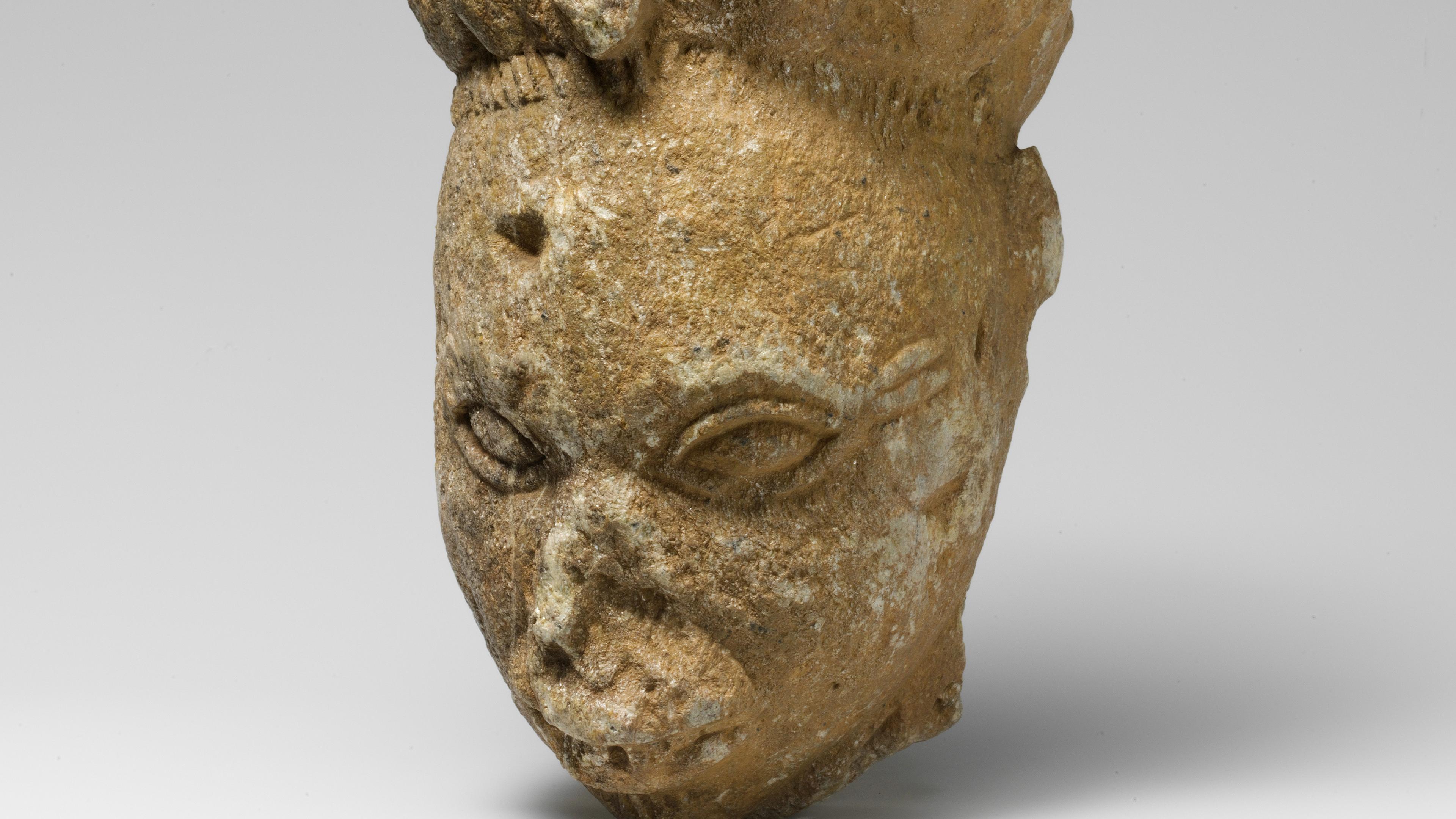 Sculpted stone head of a woman with almond eyes and scarification marks beside its left eye.