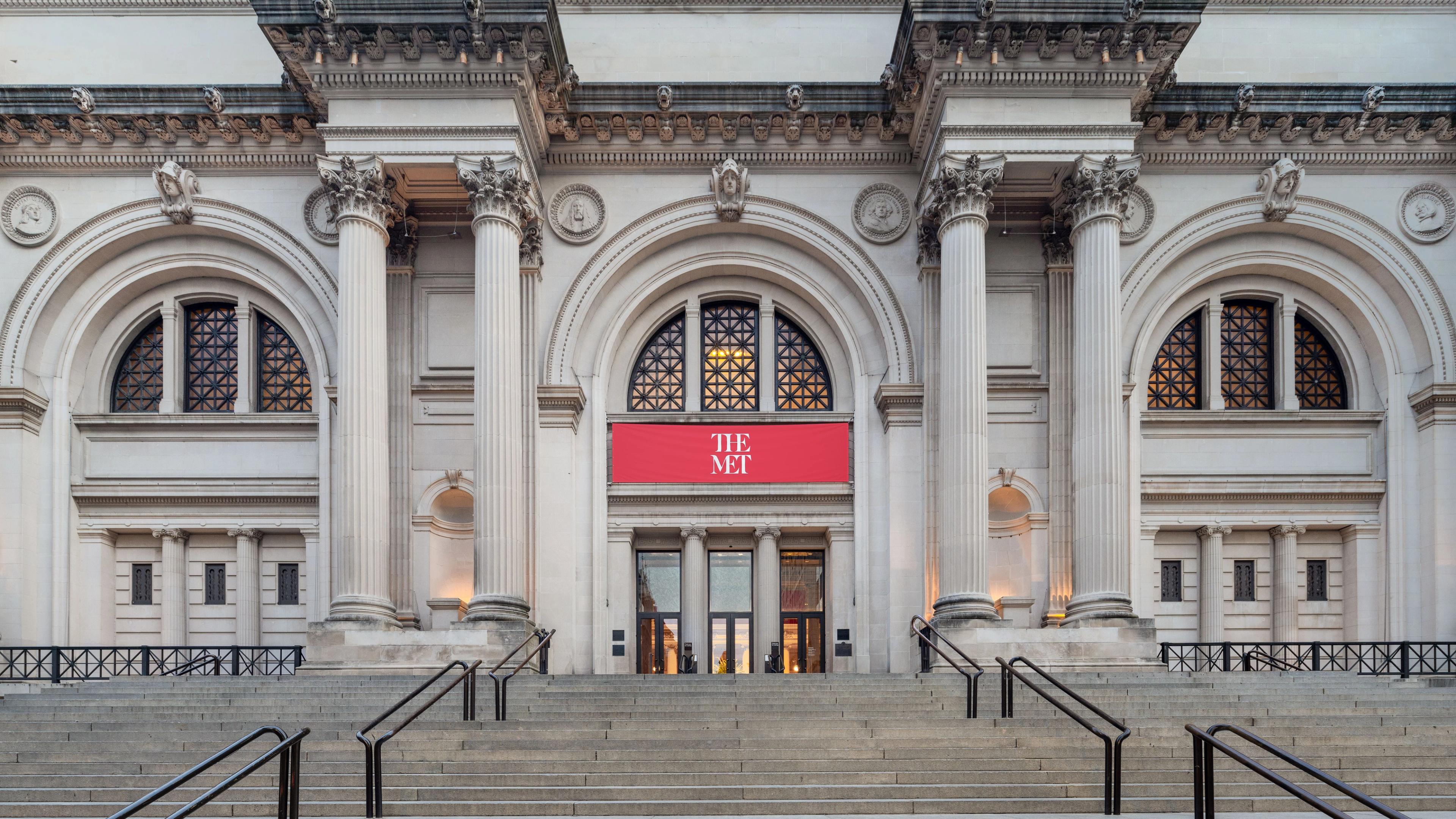 The Metropolitan Museum of Art's fifth avenue entrance on a clear day featuring tall columns and a prominent red banner displaying "THE MET."