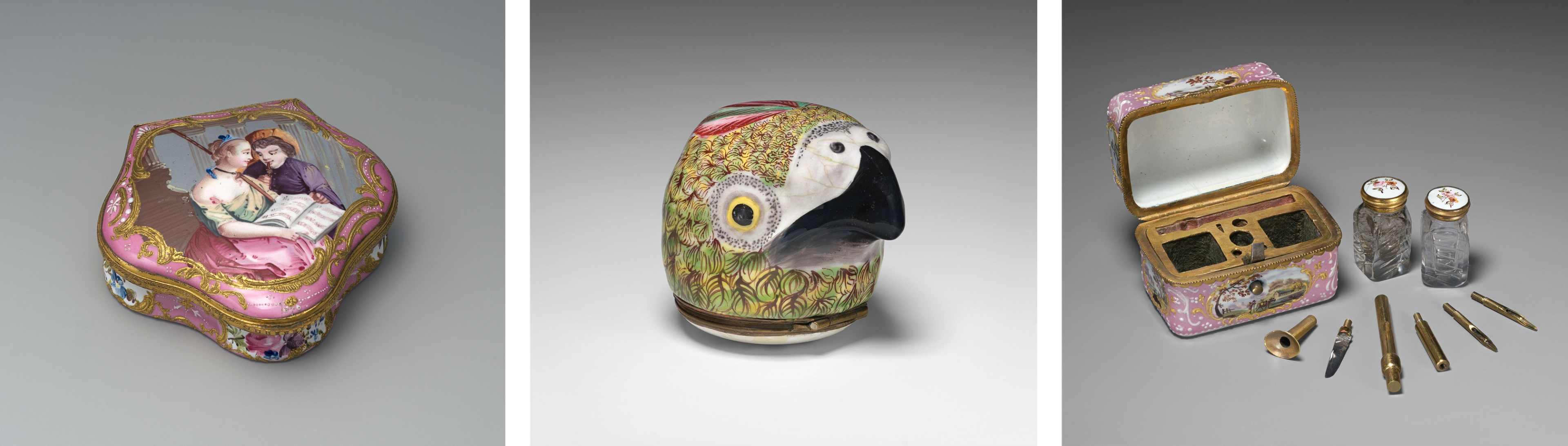 Three enameled objects. At left, a snuffbox depicting two lovers holding music sheets. At center, a green, yellow, and pink parrot's head. At right, an opened box with writing instruments arranged in front.