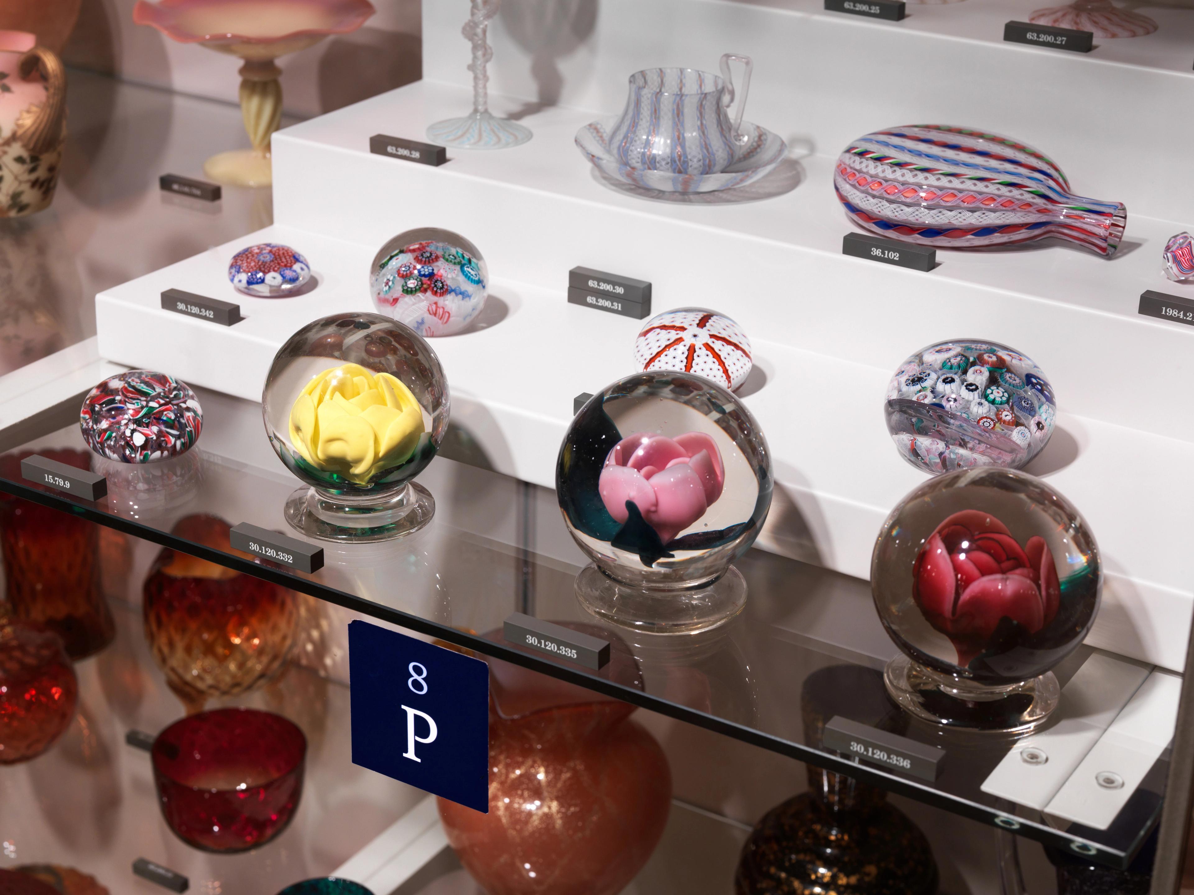 Selection of decorative glass objects displayed on shelves with identification labels.