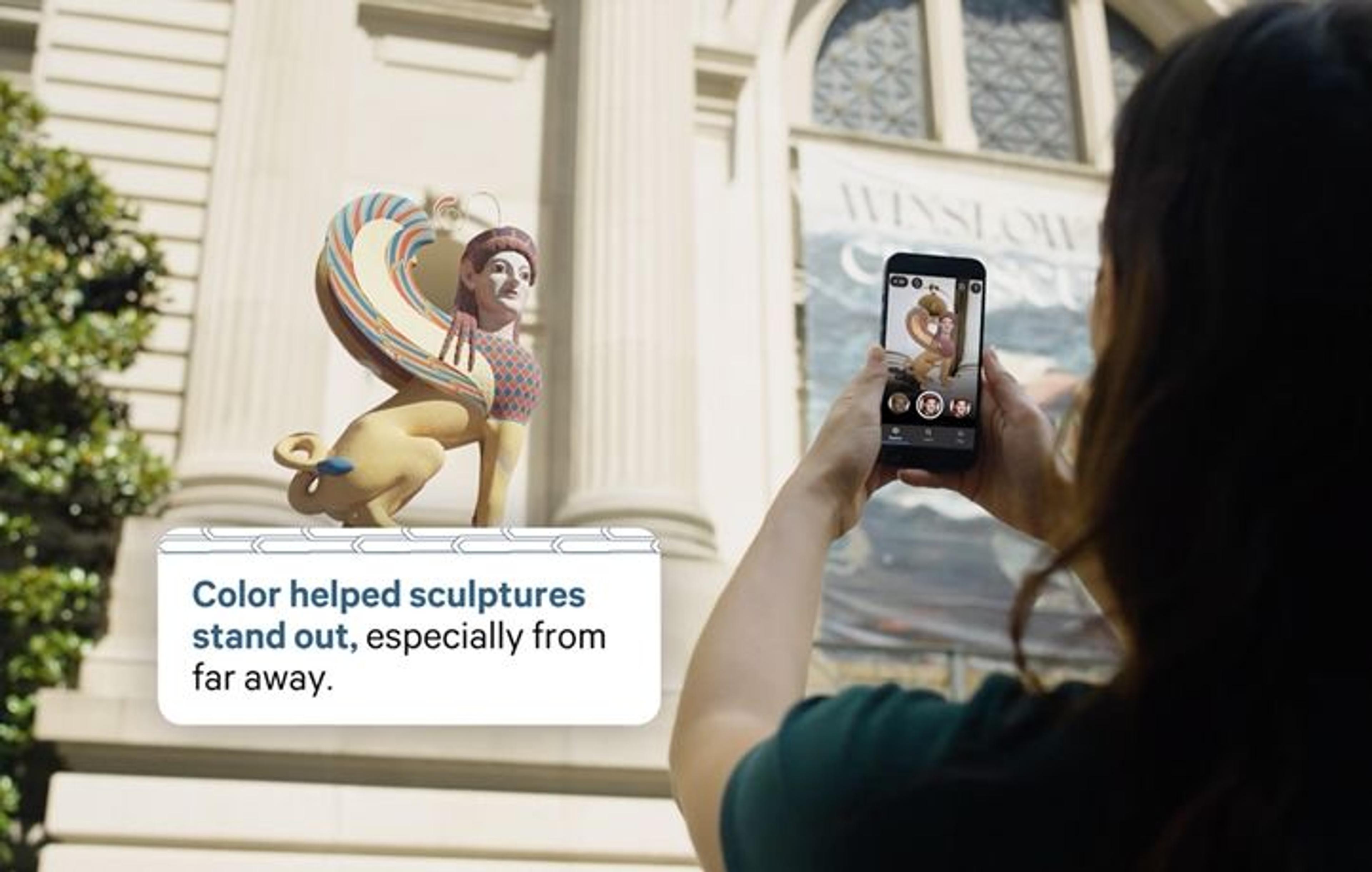 An Anciet Sculpture graphic sitting in front of the great hall entrance, with a woman in the shot holding up her phone to capture the graphic. 