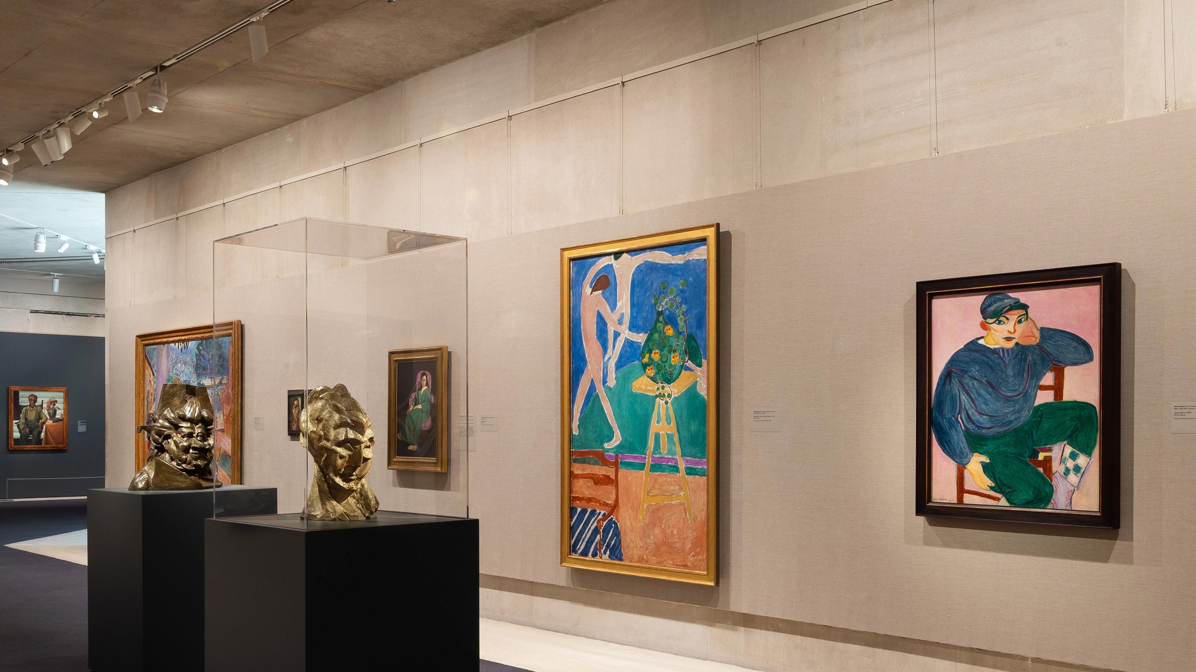Exhibit features "The Face of Life: Modern Portraits at The Met." Dimly lit room with portraits on gray walls and a sculpture on a black pedestal.