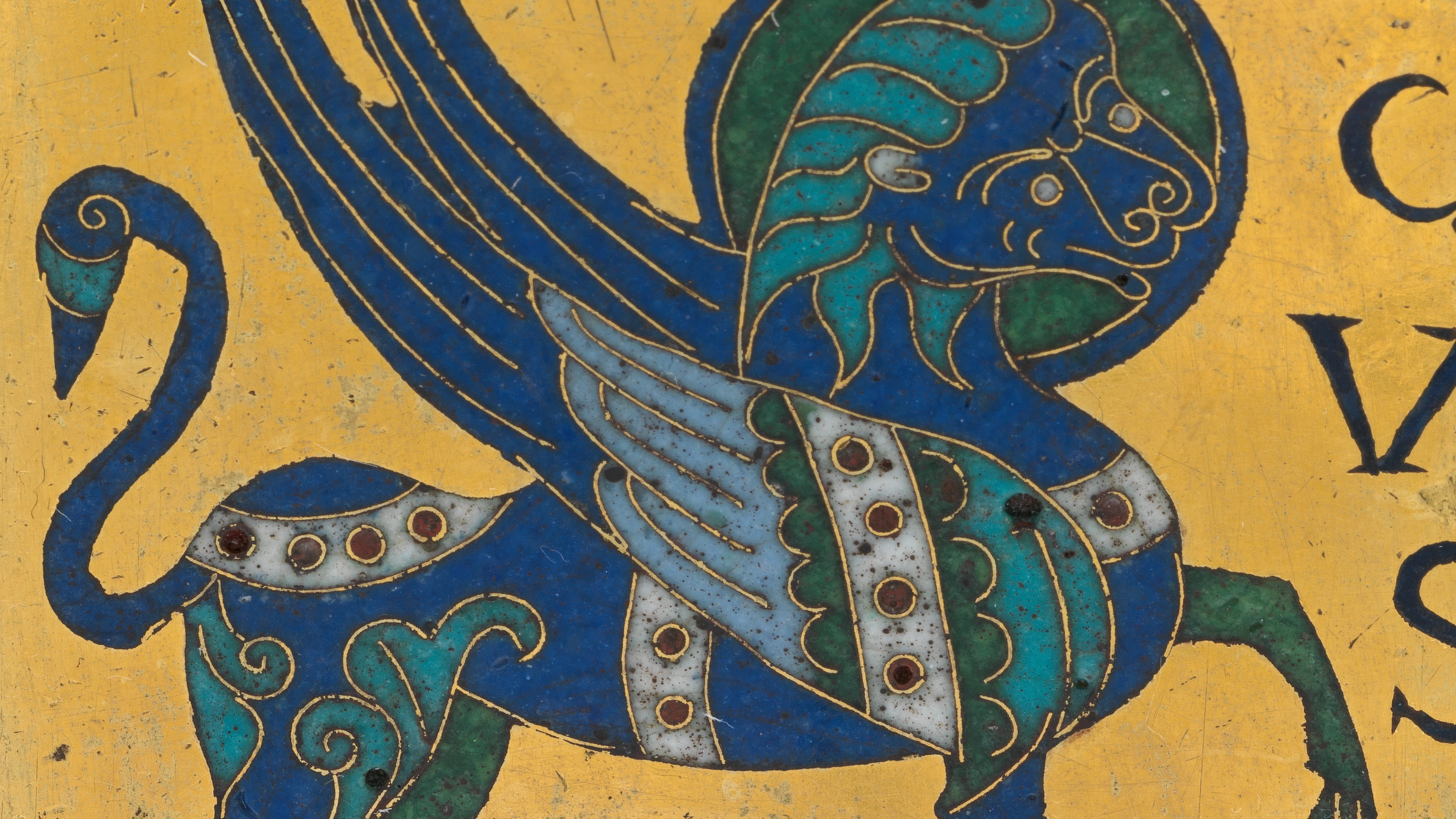 An ornate blue mythical creature with sweeping wings, curled tail, and patterned feathers fills a worn gold manuscript page beside dark decorative letters.