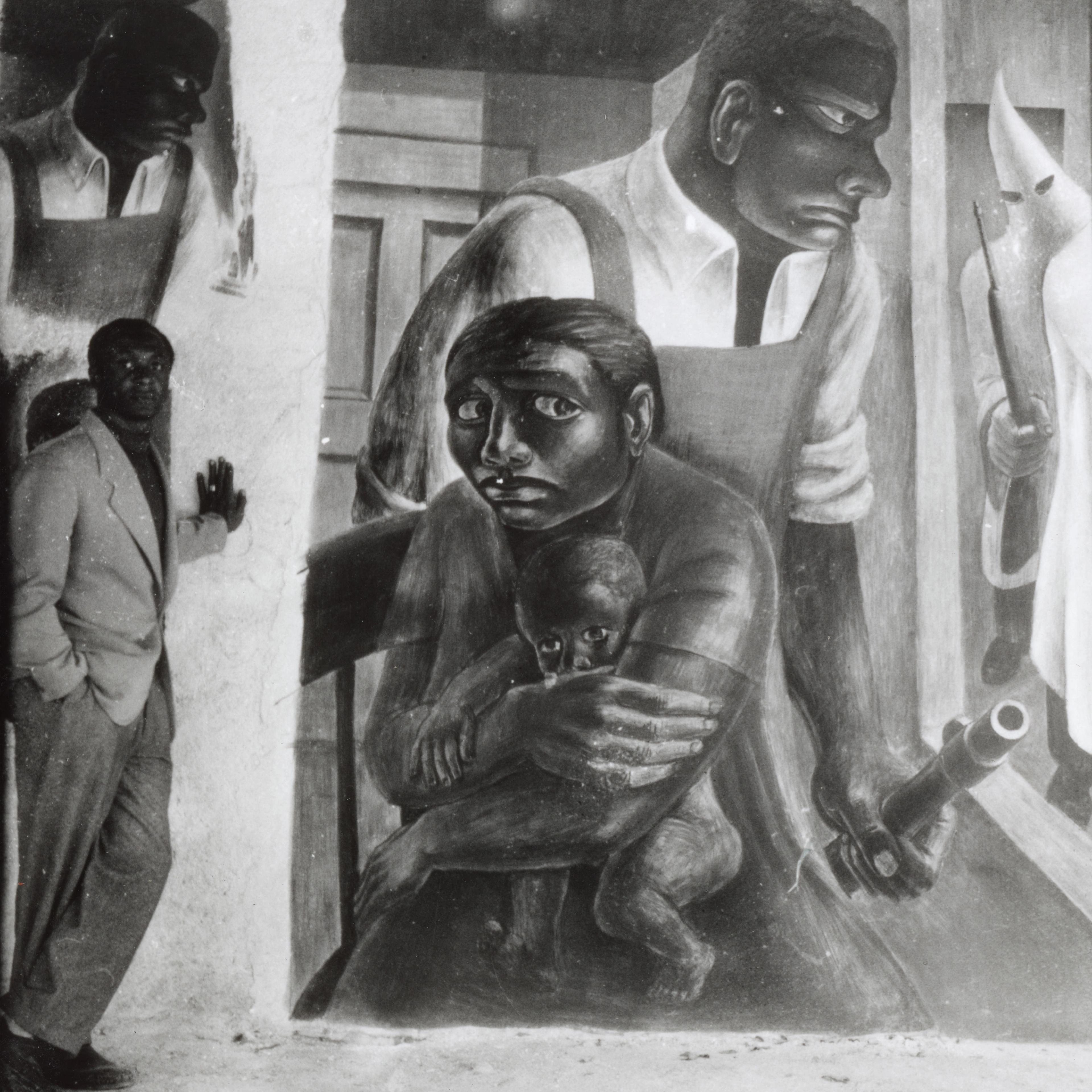 Black and white image of man standing next to mural depicted in black and white of a mother shielding her baby and while a strong black meale guards her. 