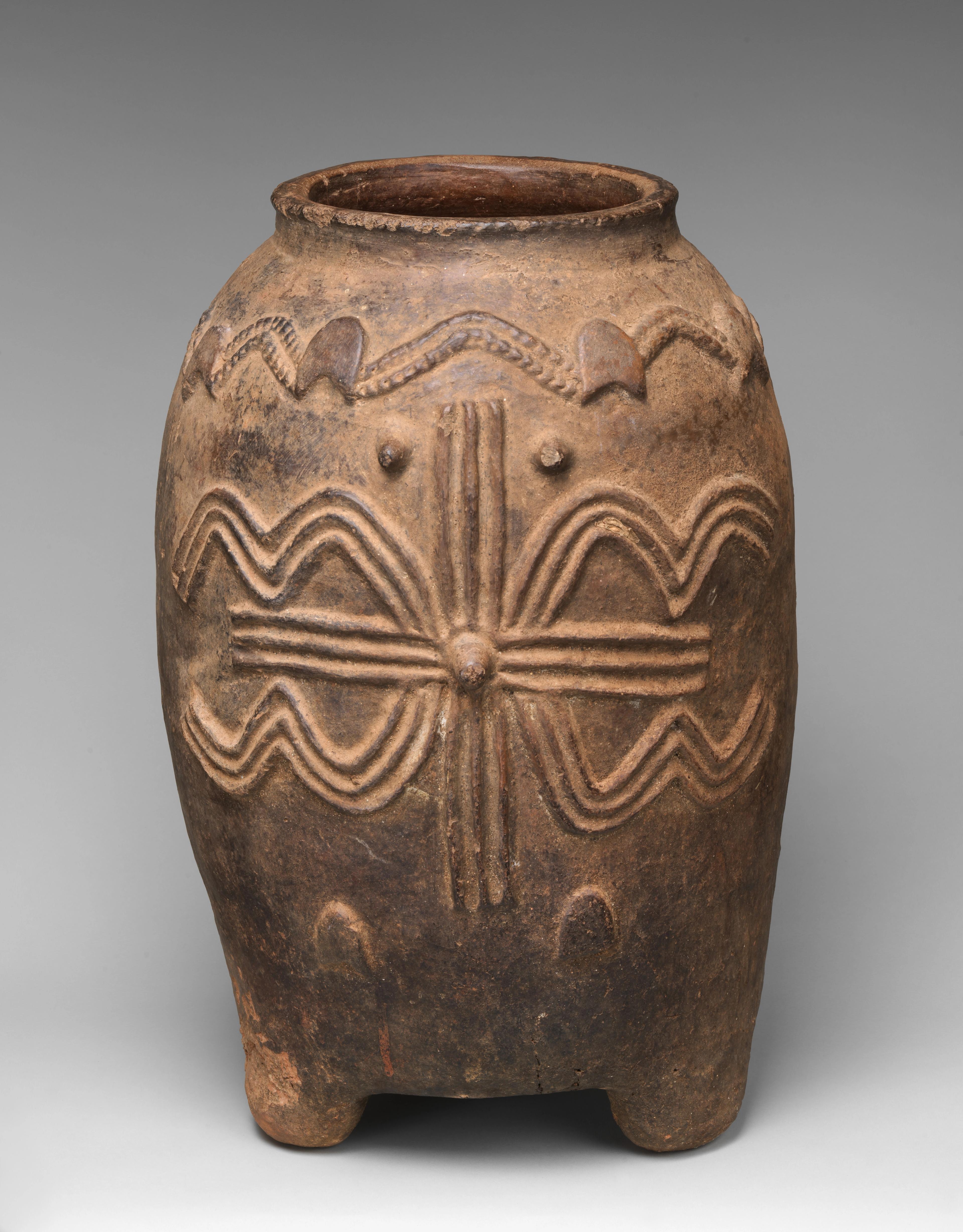 vessel on four short legs, decorated with patterns of raised lines and circles.