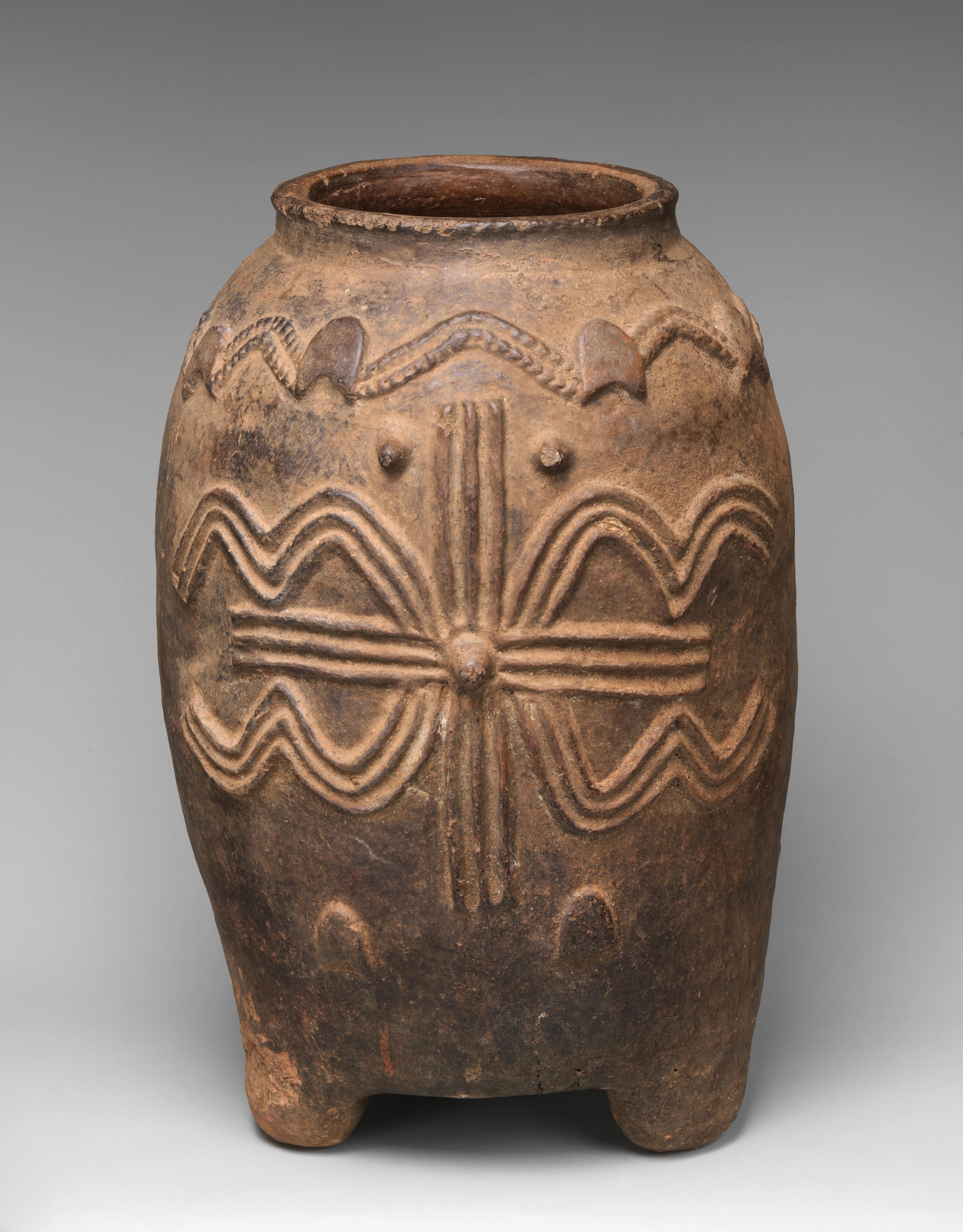 vessel on four short legs, decorated with patterns of raised lines and circles.