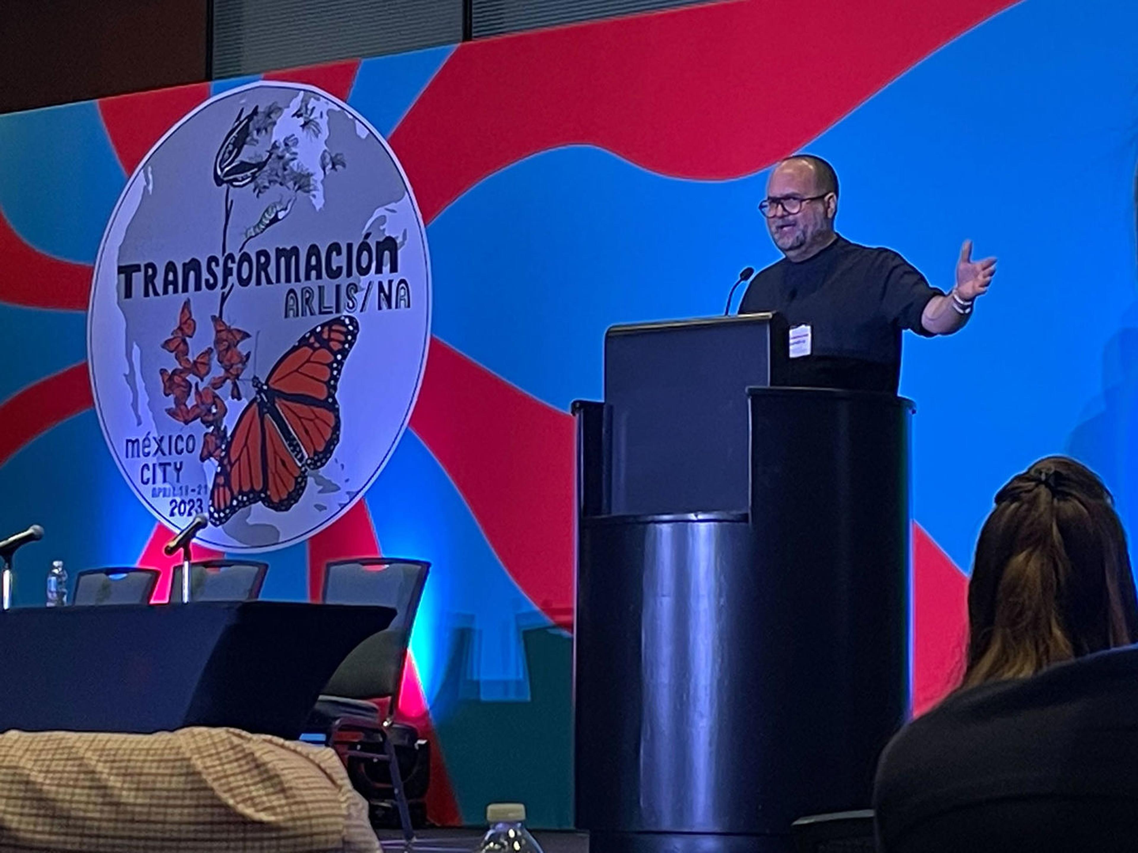 Alejandro Cartagena  speaking in front of a colorful background