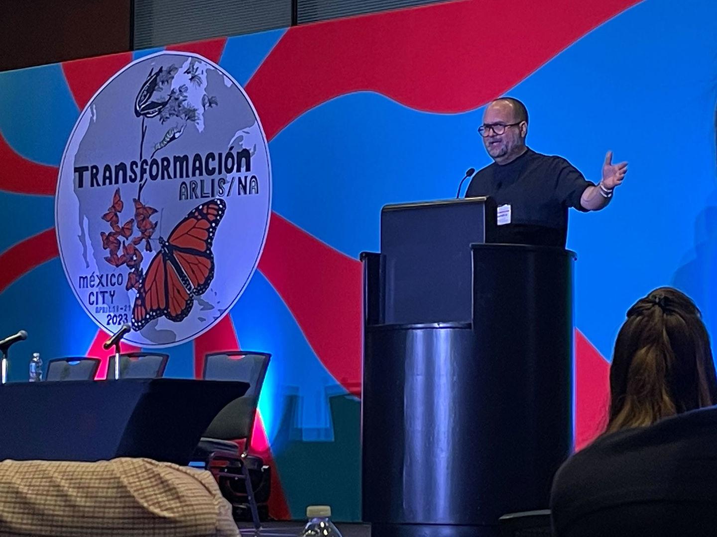 Alejandro Cartagena speaking in front of a colorful background