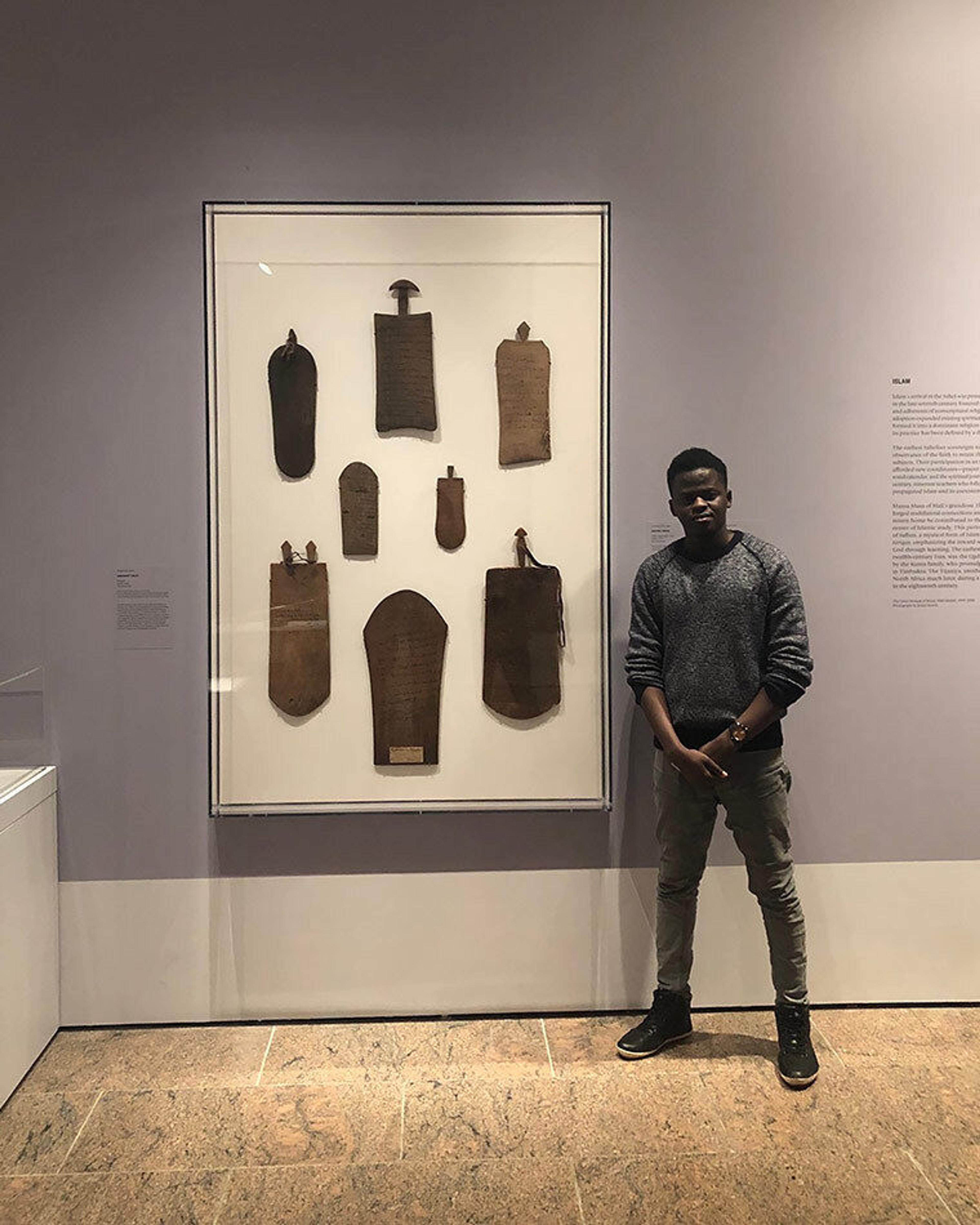 A man stands next to a white frame hanging against a lilac wall, encasing eight thin slabs of wood.