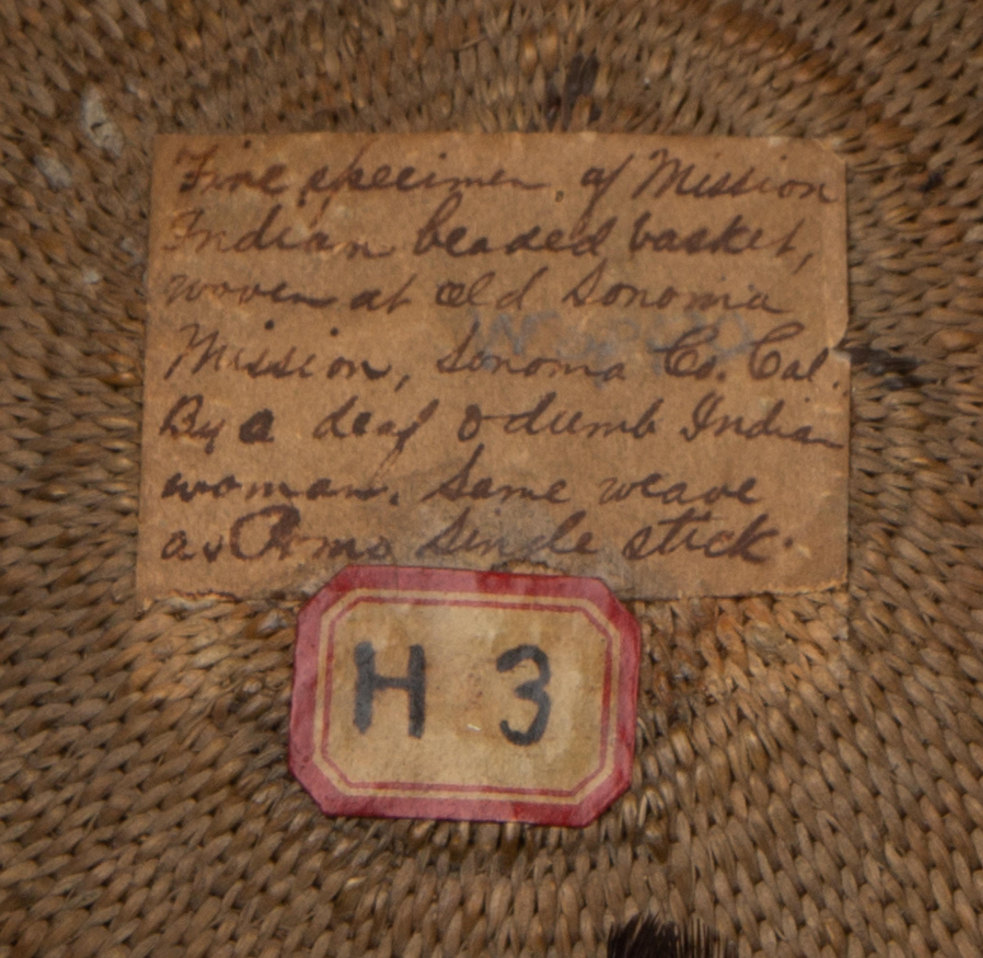 a sticker affixed to the inside of a basket reading: "Fine specimen of Mission Indian beaded basket, woven at Old Sonoma Mission, Sonoma, Co. Cal, By a deaf and dumb Indian woman, Same weave as Pomo single stick.