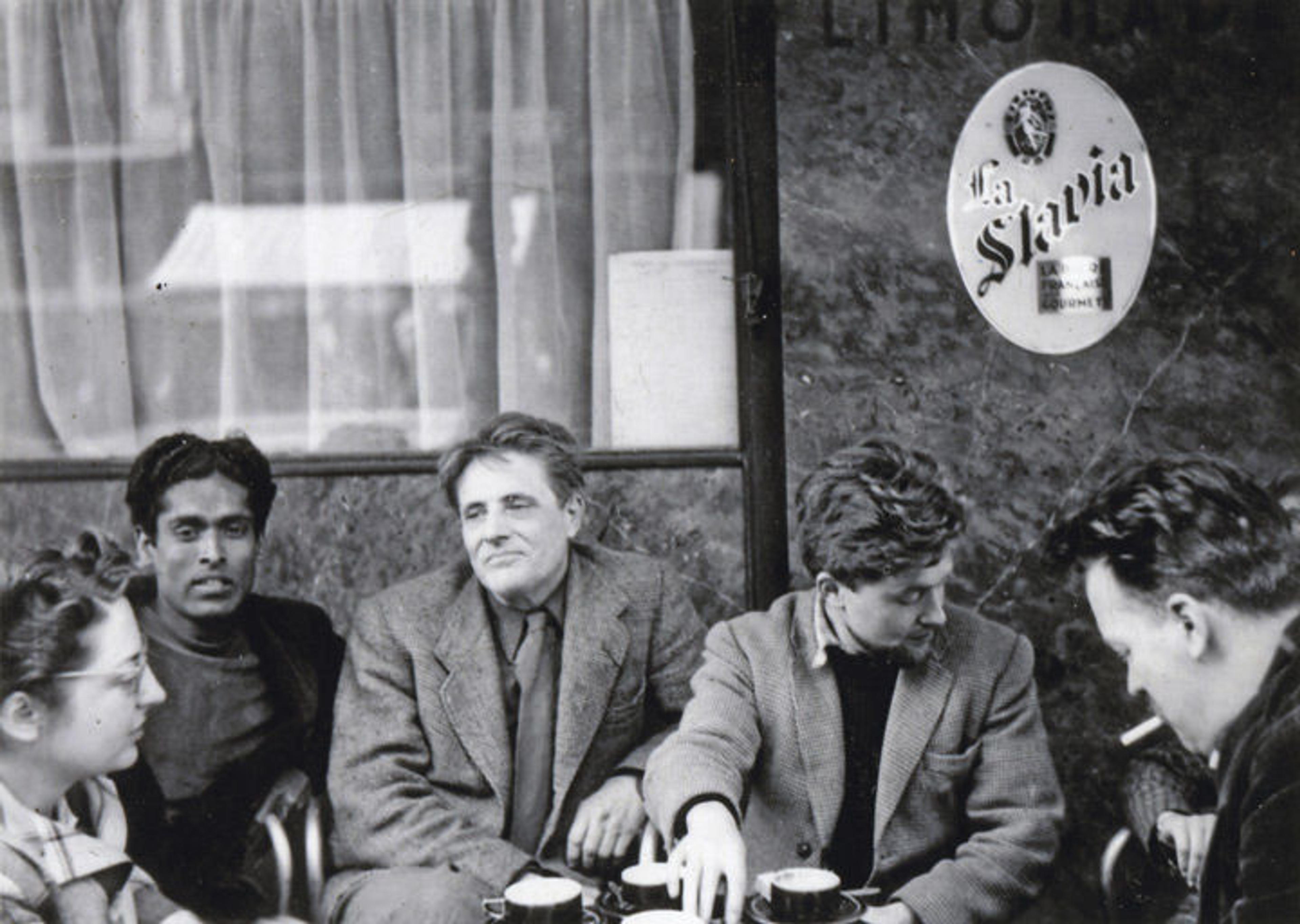 Black-and-white photo of a group of artists sitting and talking around a table at a cafe in Paris