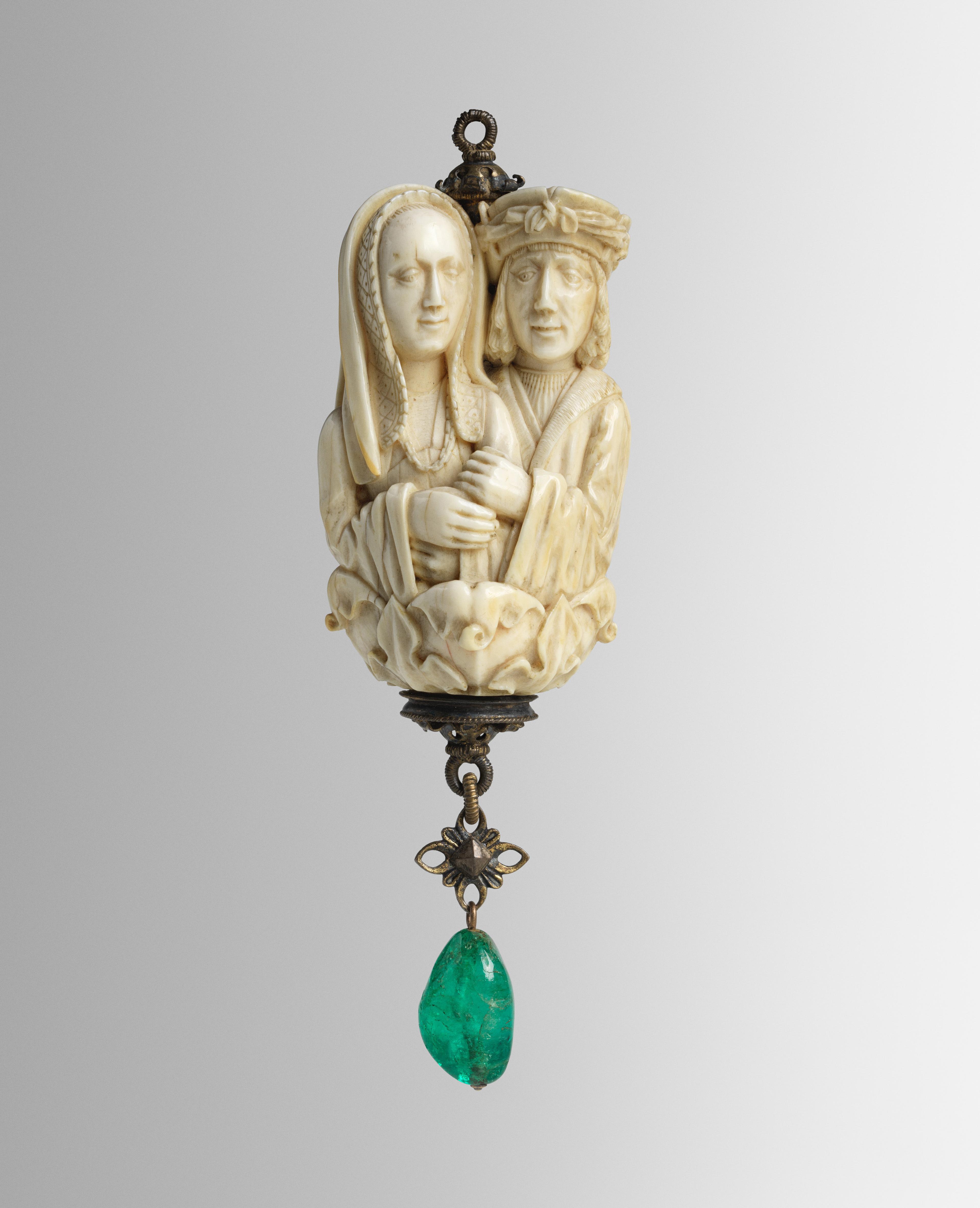 An ivory rosary terminal bead carved with two lovers with an emerald pendant attached at the bottom.