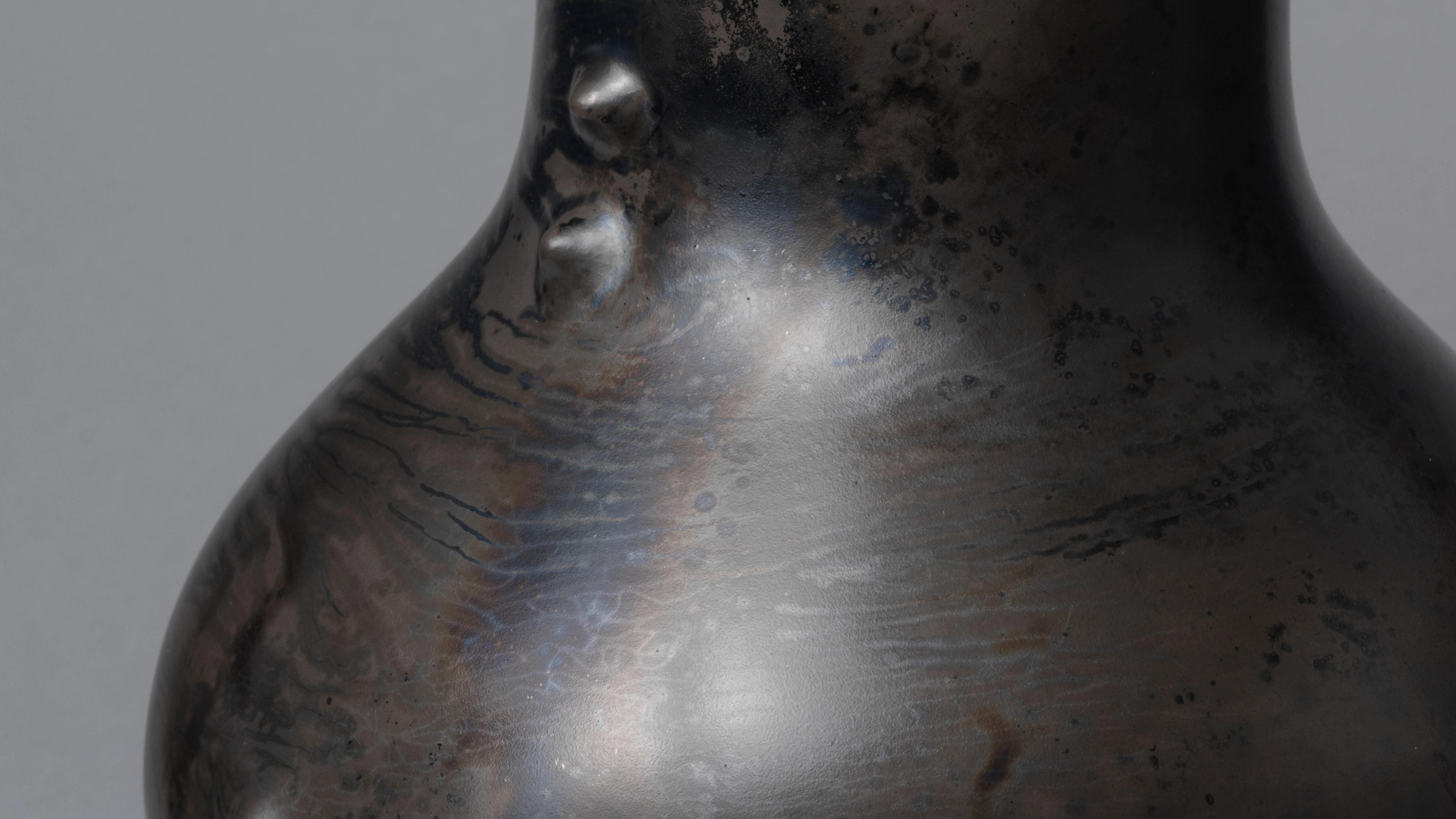 Detail of a black ceramic vessel with a shiny, burnished surface and two small raised bumps at the base of the neck.