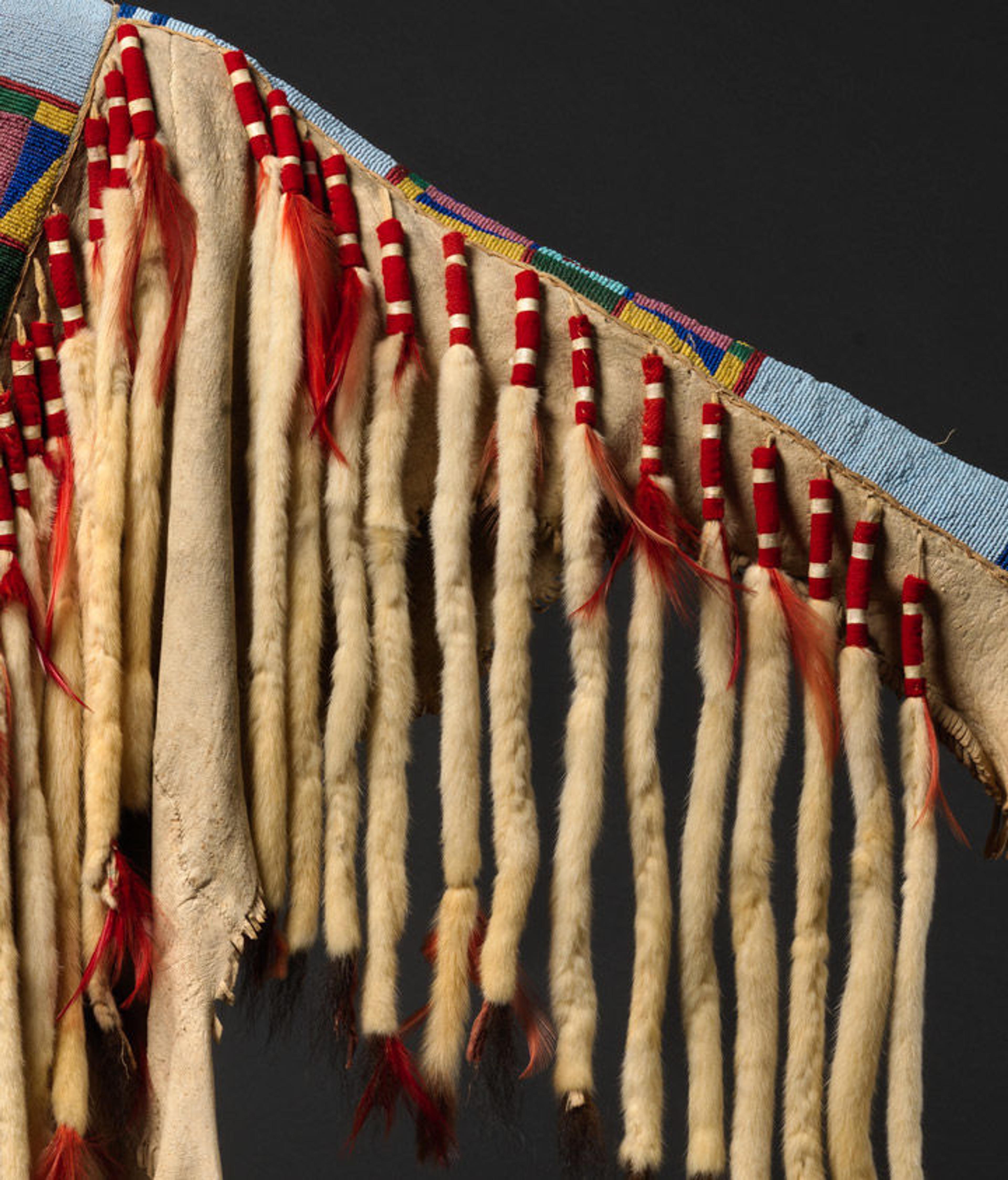 A closeup image of a Crow war shirt from 1880, focusing on the strips of white ermine fur sewed onto the sleeve