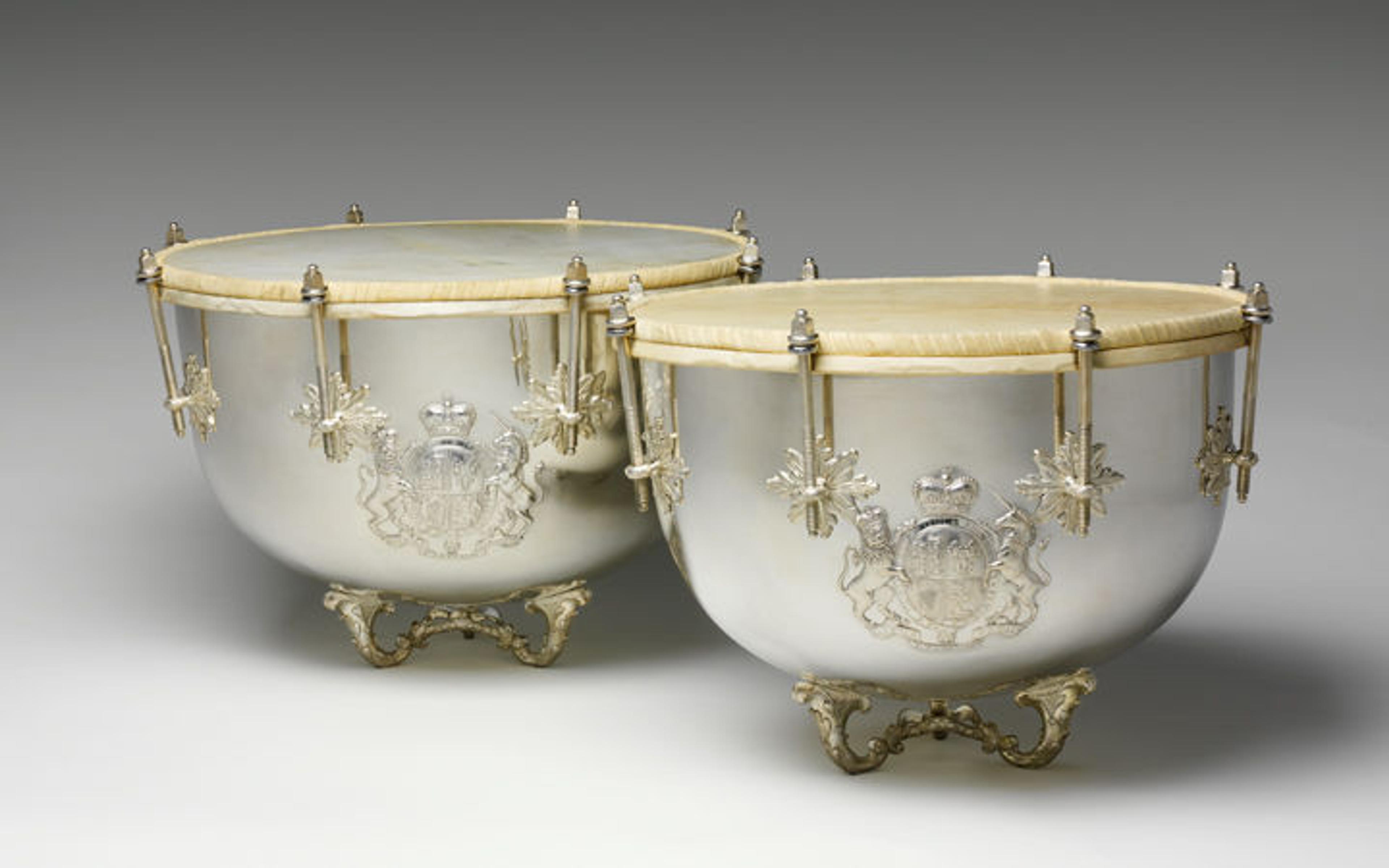A pair of solid silver kettledrums with ornate bases and heraldic coats of arms