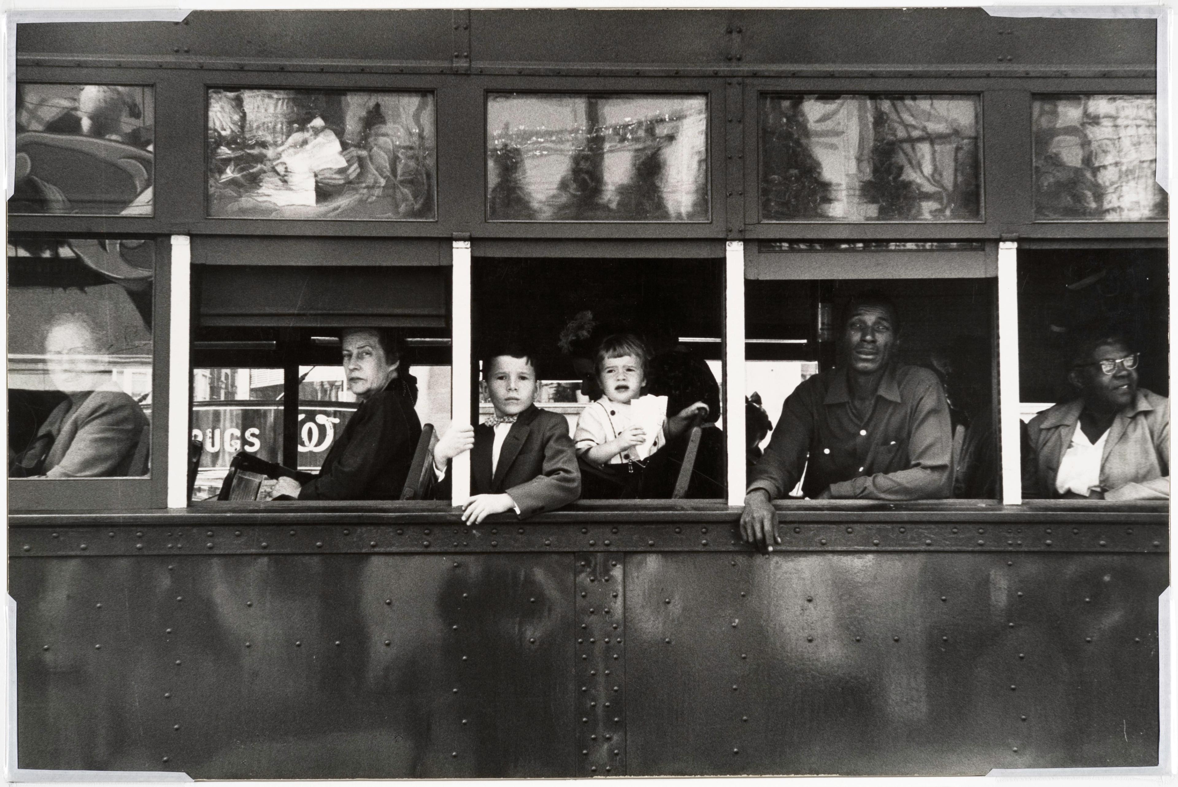 Black and white photograph of people looking out the windows of a trolley.