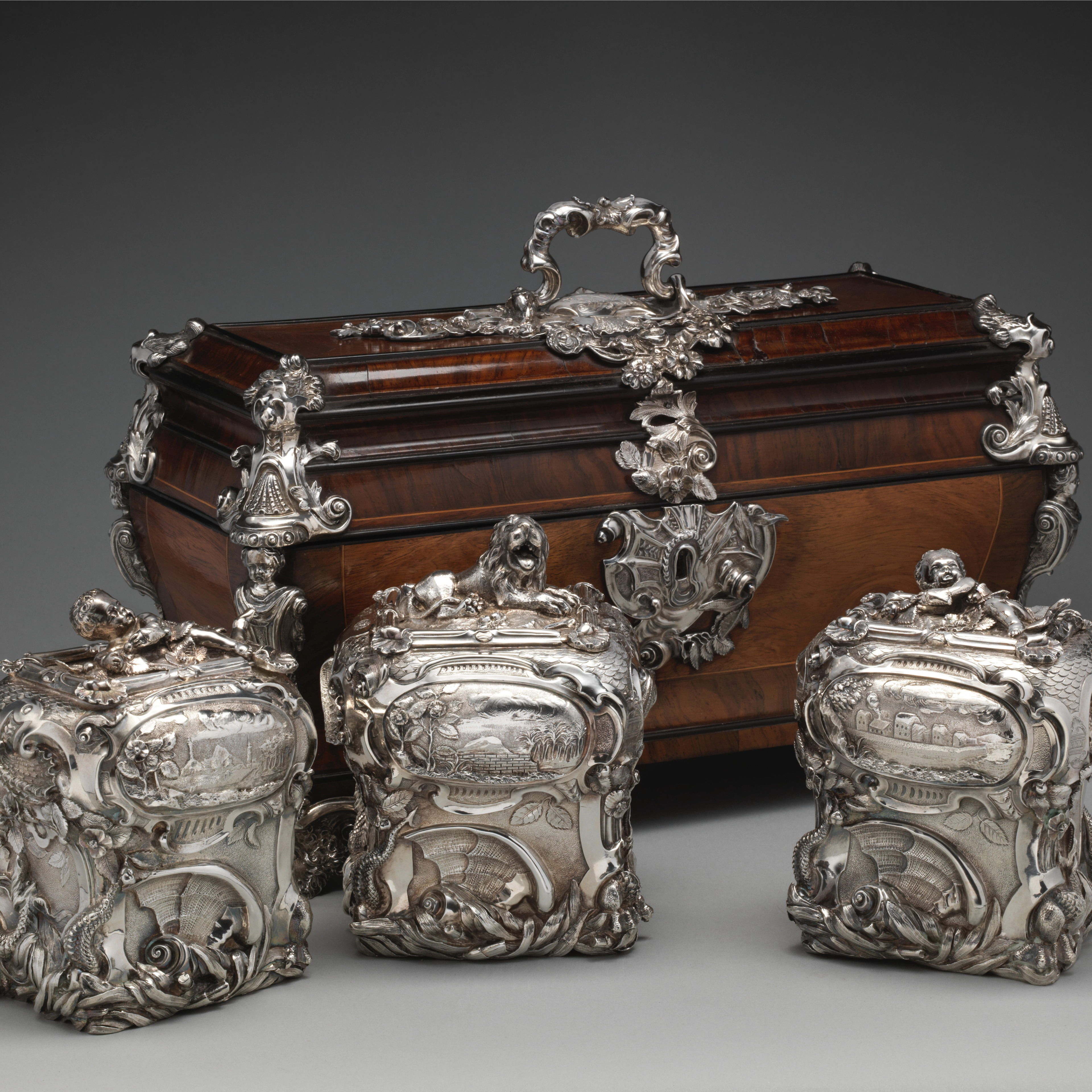 Silver pair of tea caddies and sugar box in front of a matching wooden case.
