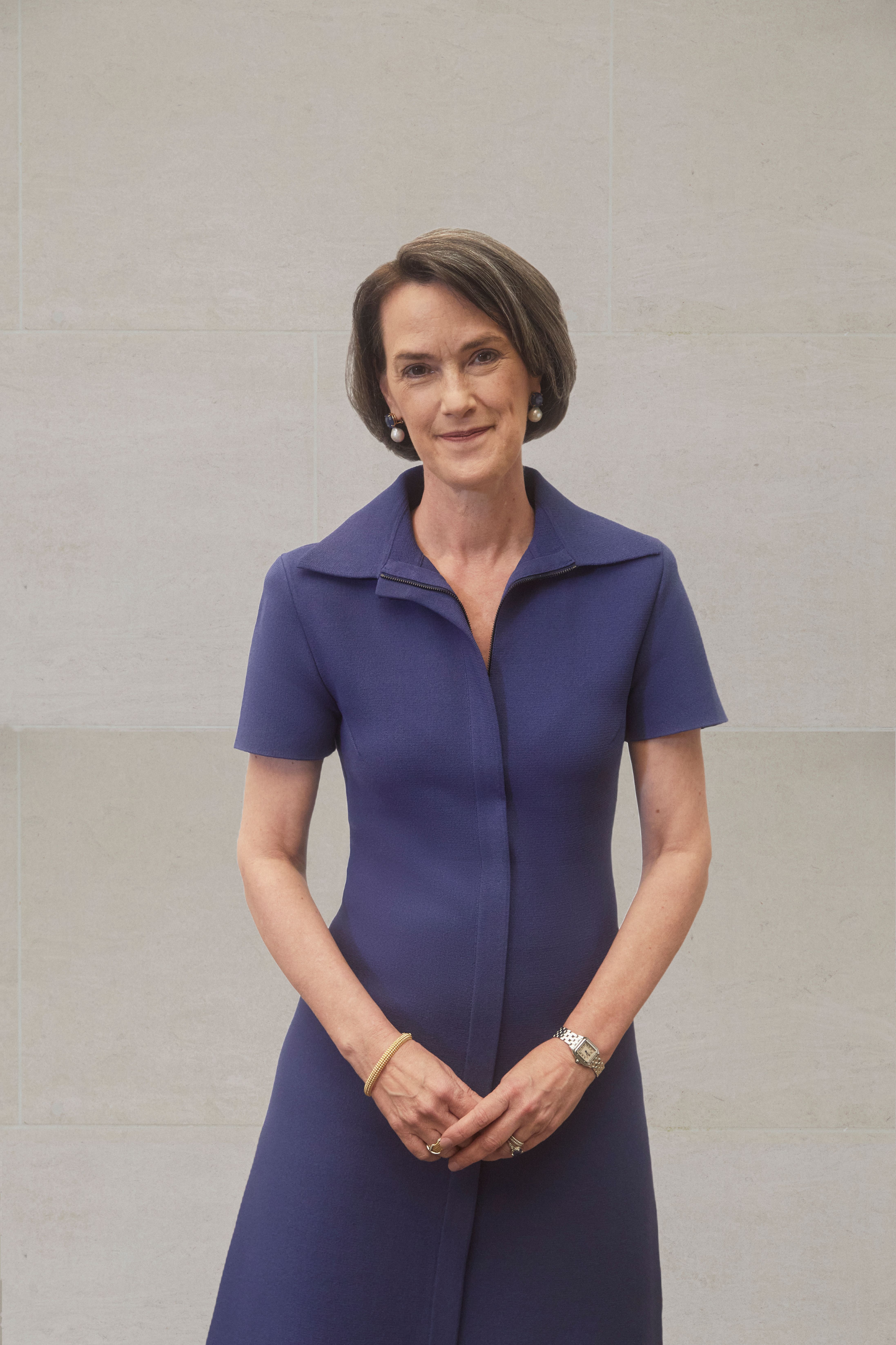 A color photograph of Whitney Donhauser standing in front of a stone wall in a dark purple dress.