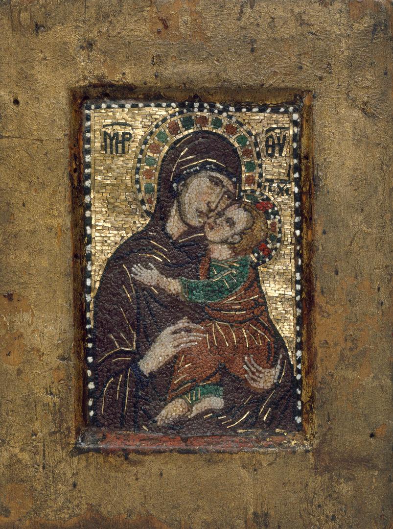 A byzantine miniature mosaic of the virgin and child. On the left the virgin holds christ wearing dark brown robe with a patterned halo around her hooded head. On the right is the child christ in a brown and green rob clutching his mother. The are flanked by Cyrillic characters and the background is gold mosaic.