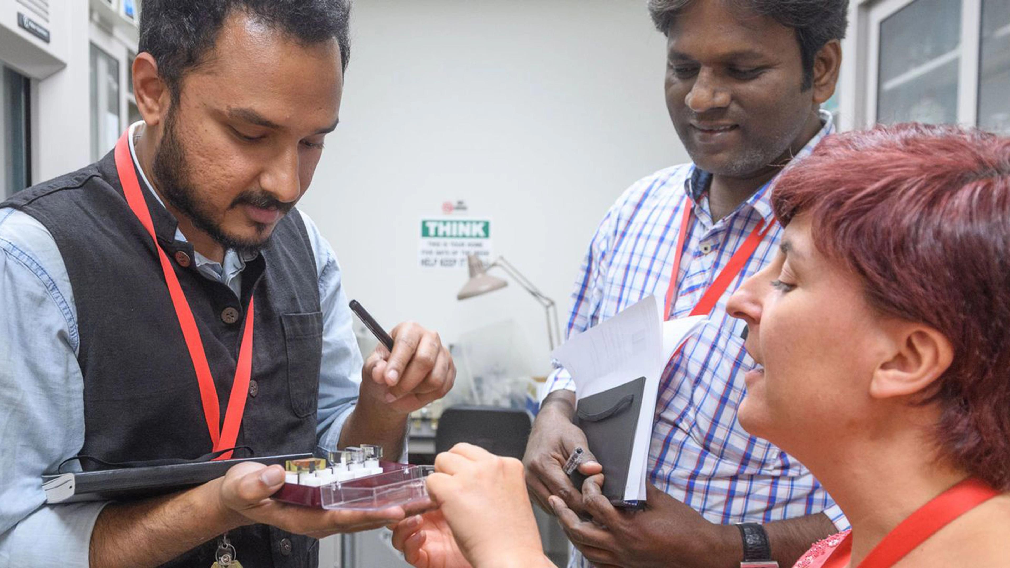 Three people standing in a lab, looking at a sample in one figure's hand.