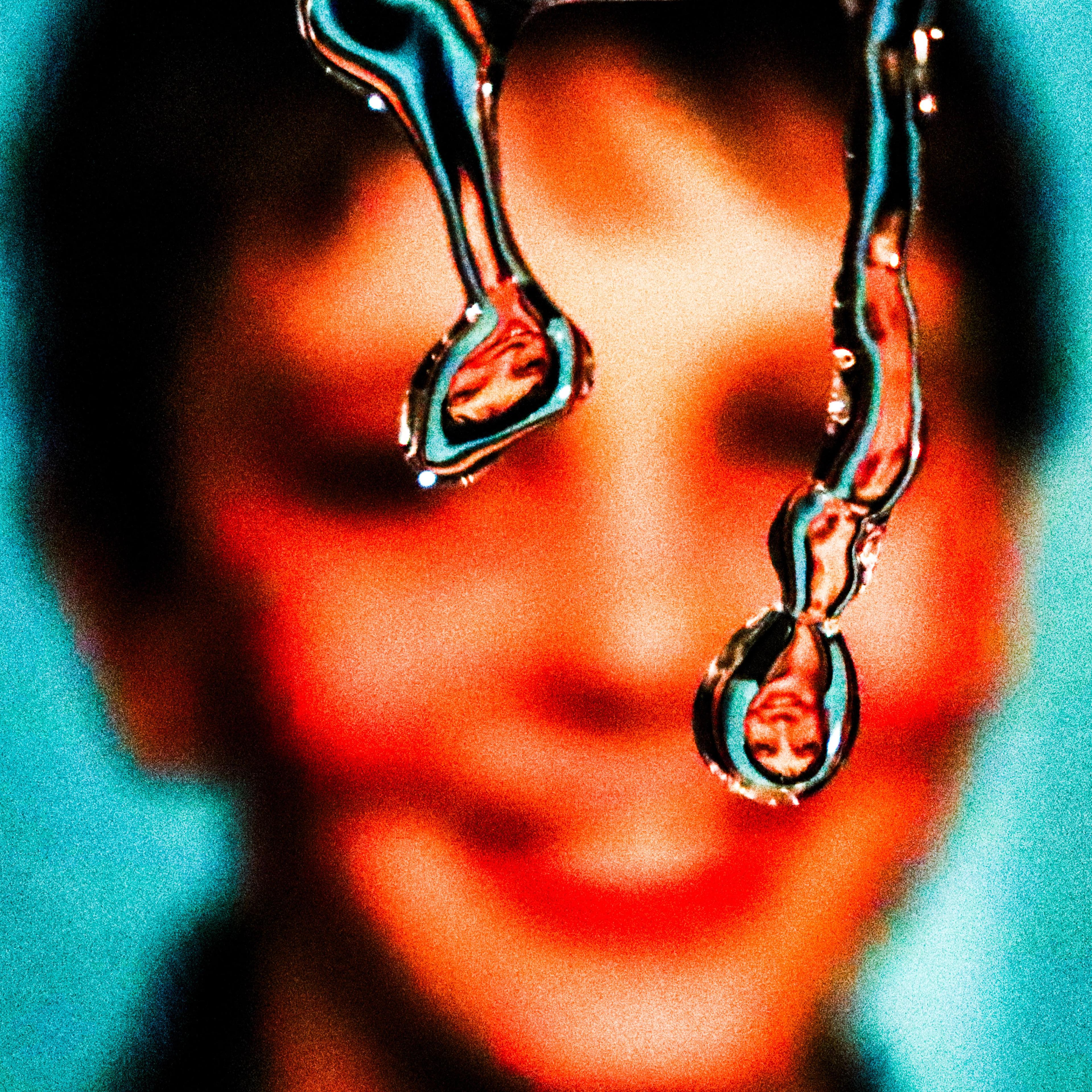 Close-up of two liquid-like droplets reflecting an upside down image of a smiling face in the background.