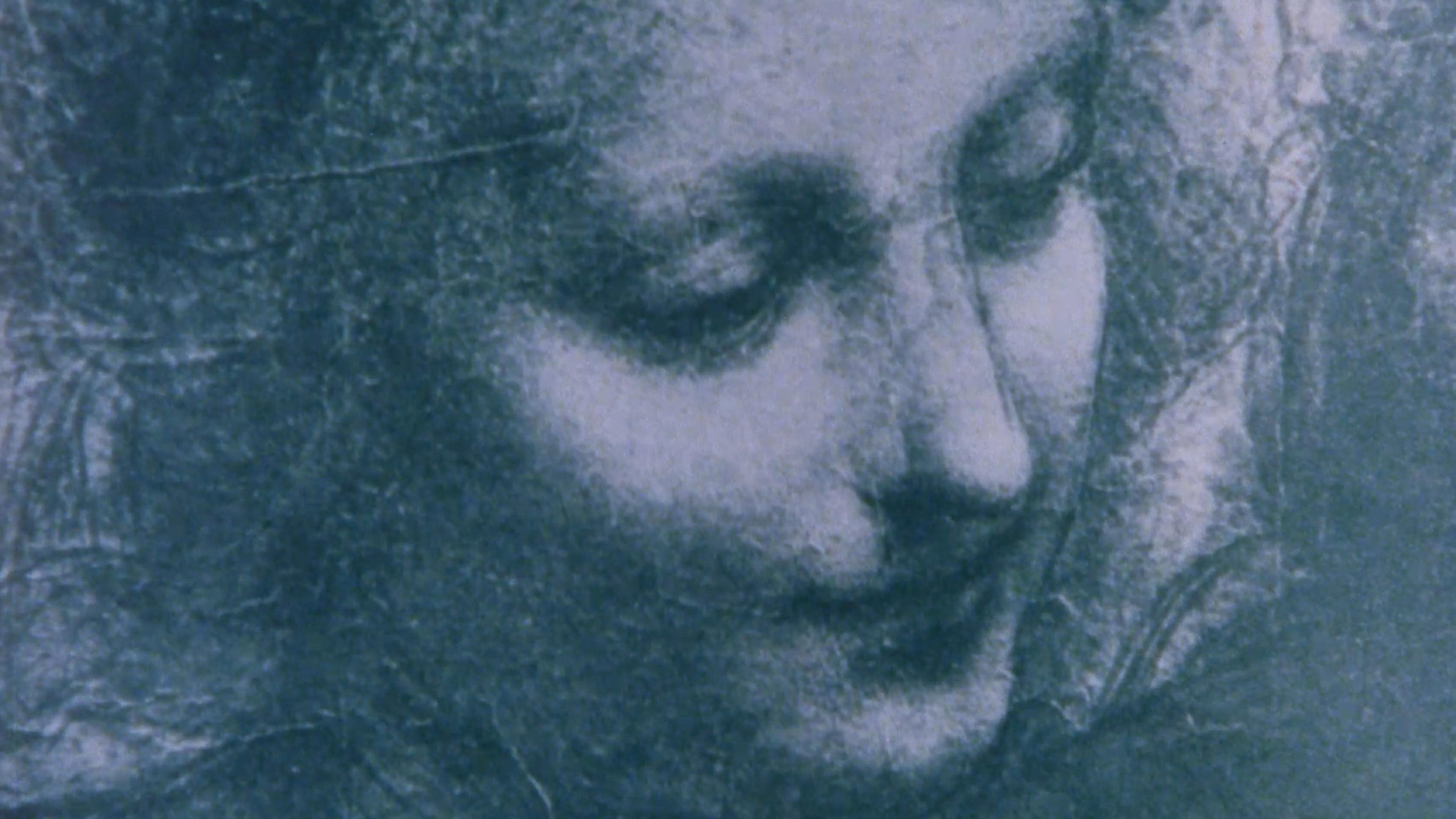 Blue-toned close-up portrait of a bearded person with eyes closed, conveying a quiet, introspective mood through grainy, textured lighting.