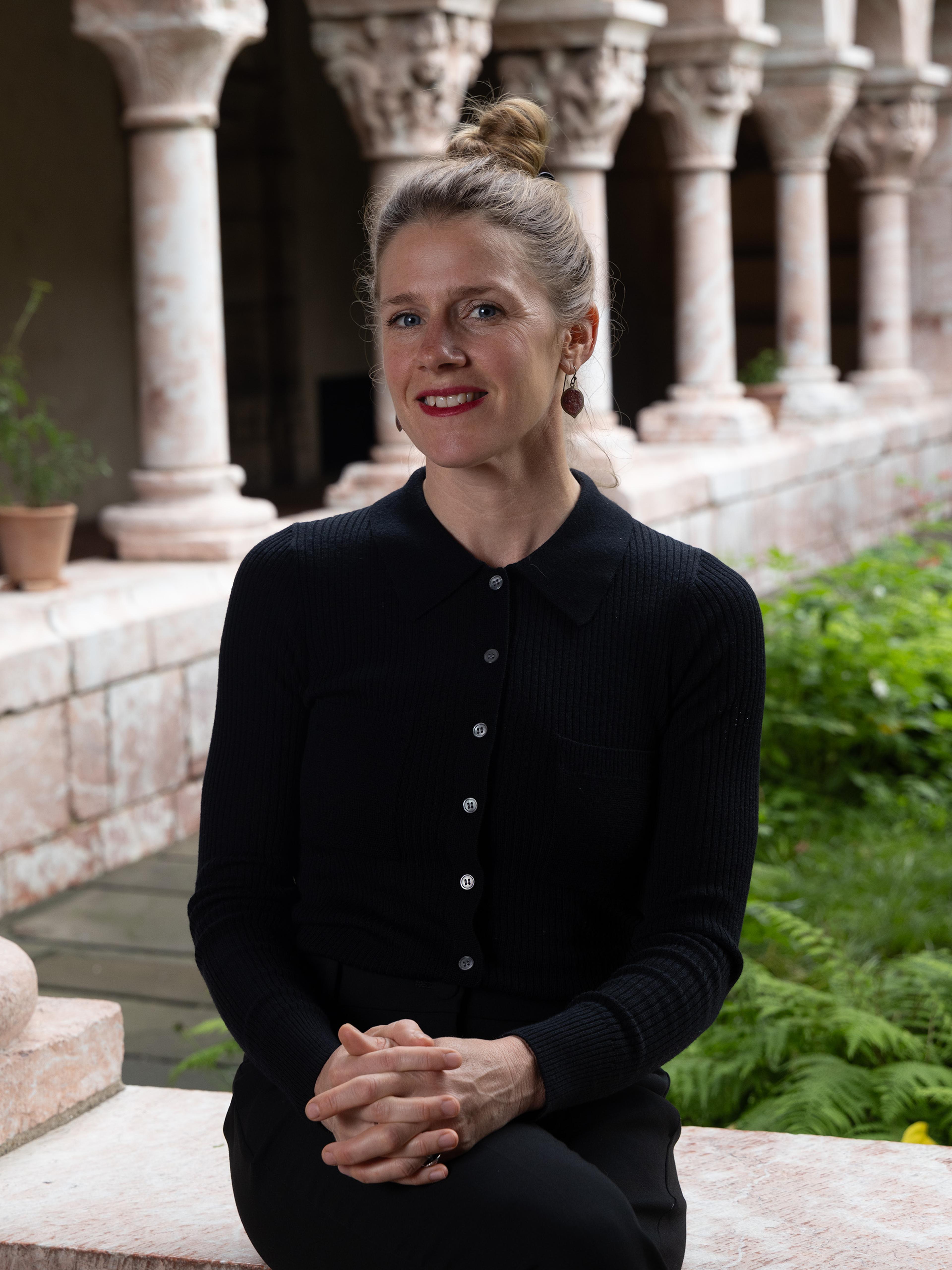 A woman wearing a black blouse sits in front of a marble arcade