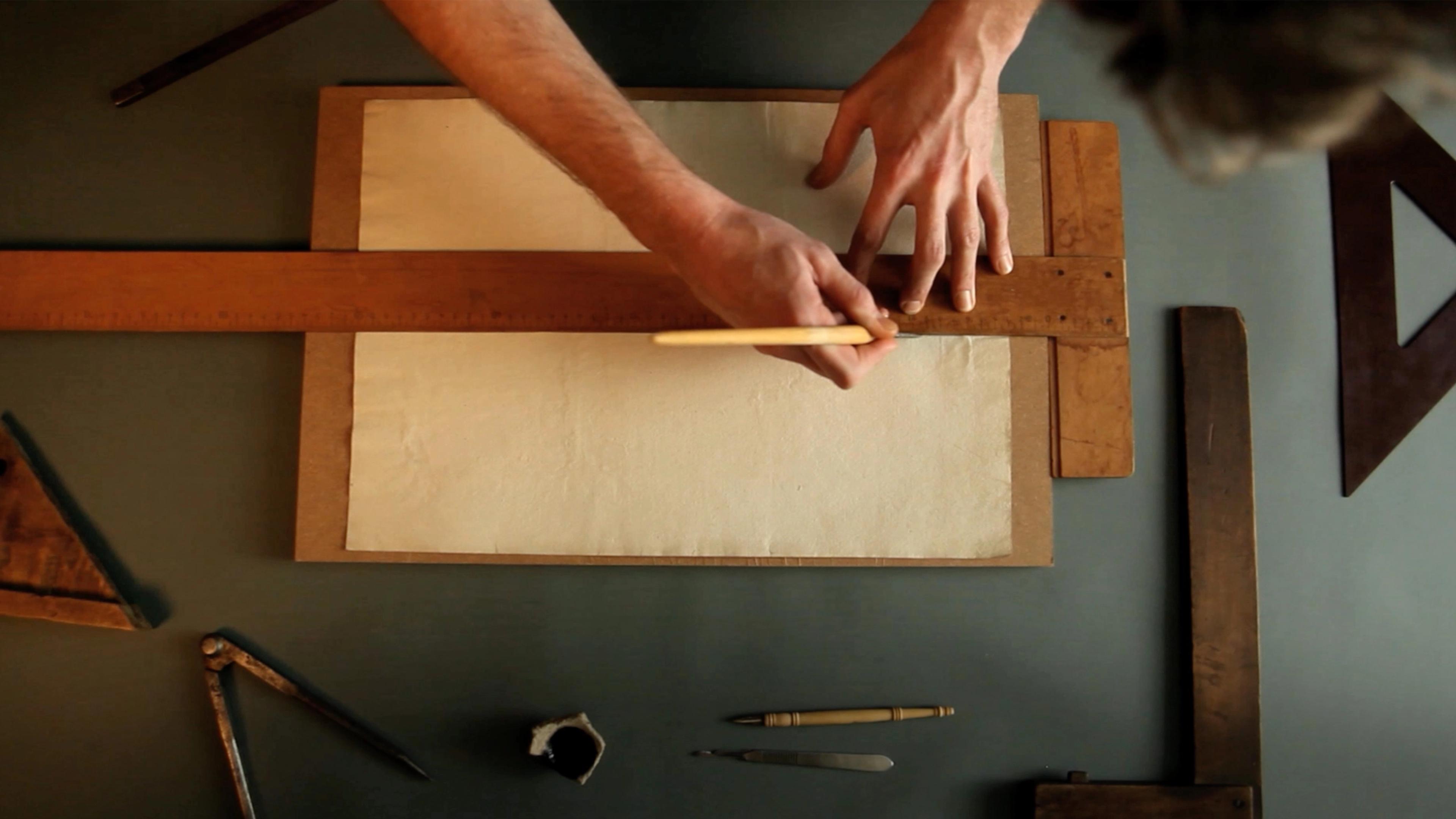 Hands measure paper using a ruler on a drafting table. Surrounding tools include a triangle, compass, and pencil, conveying a focus on precision.