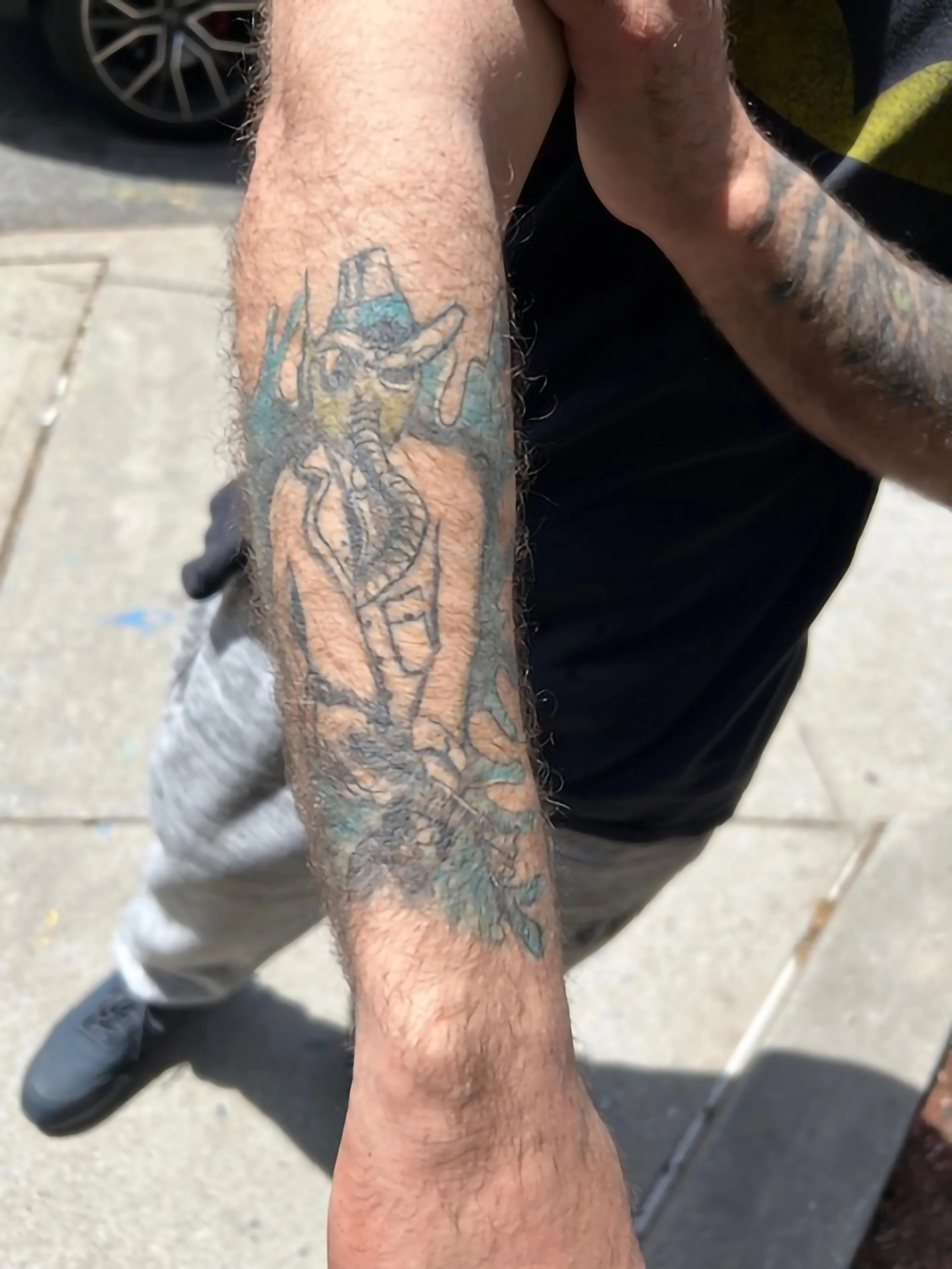 Forearm tattoo showing a figure in a gas mask, flanked by blue flames.