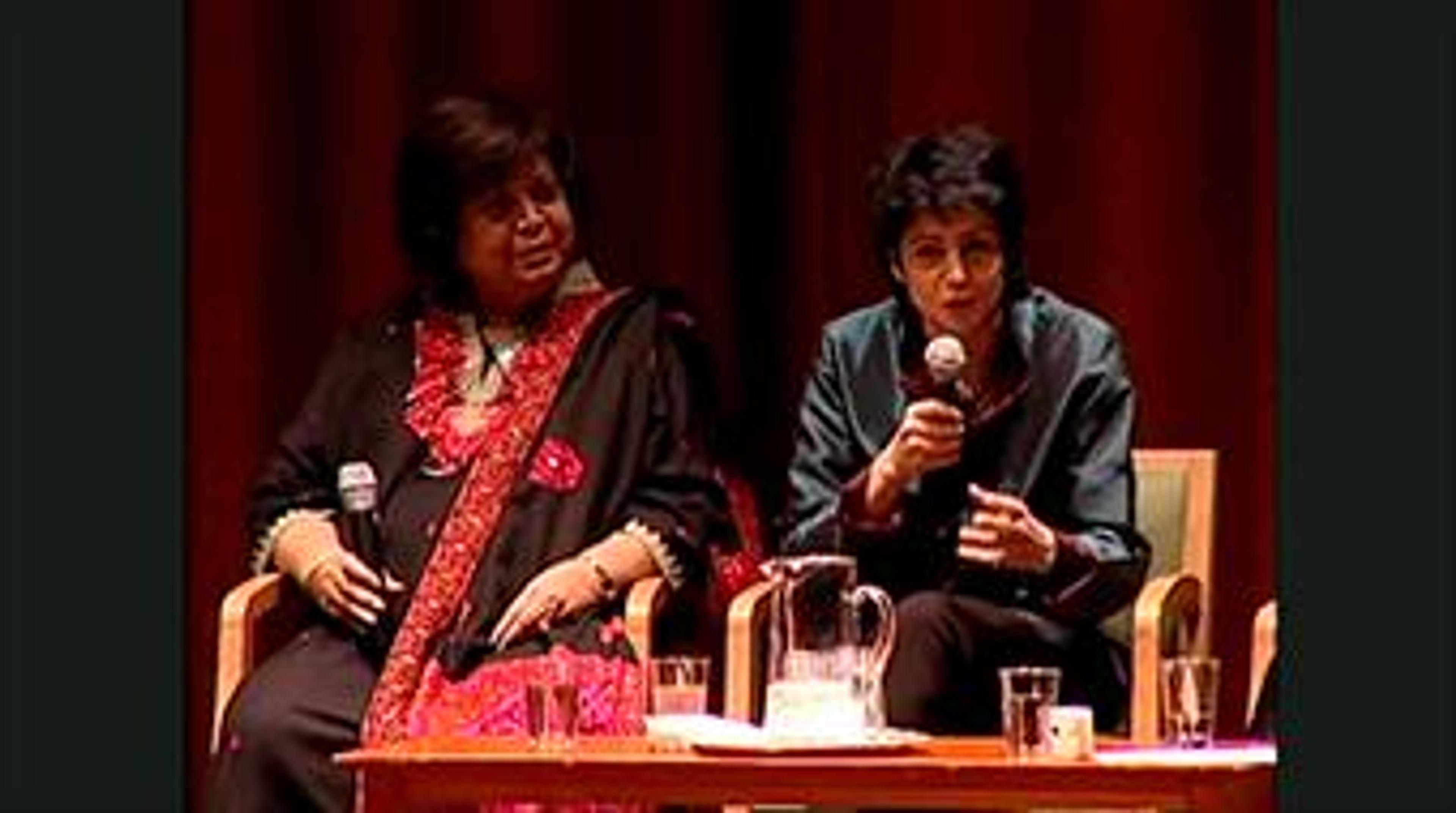 Two women sitting on a stage holding a microphone