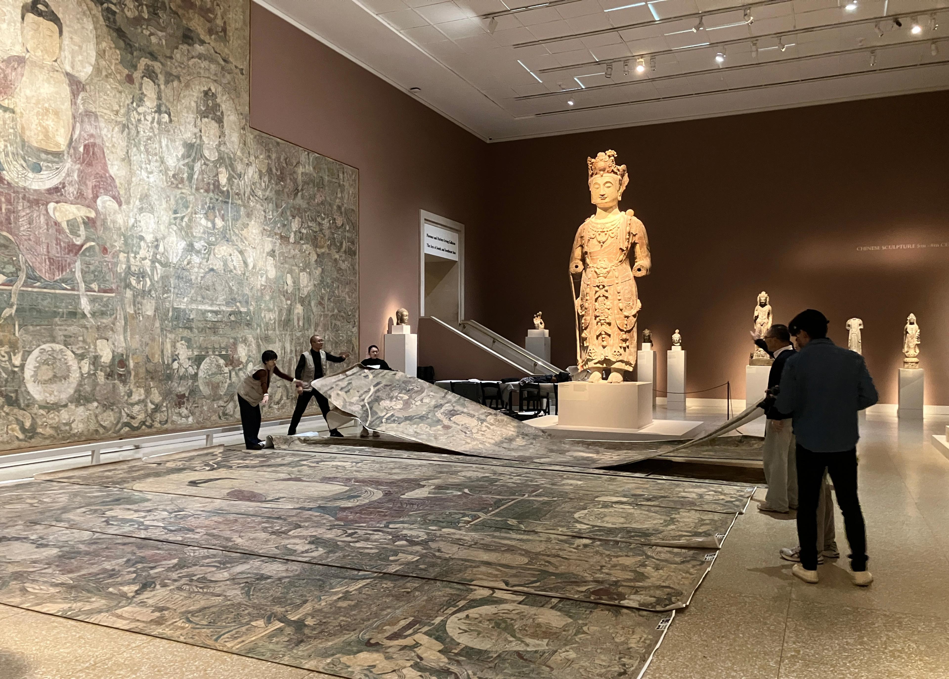 In gallery view of the large-scale Buddha painting being assembled on the floor by several people.