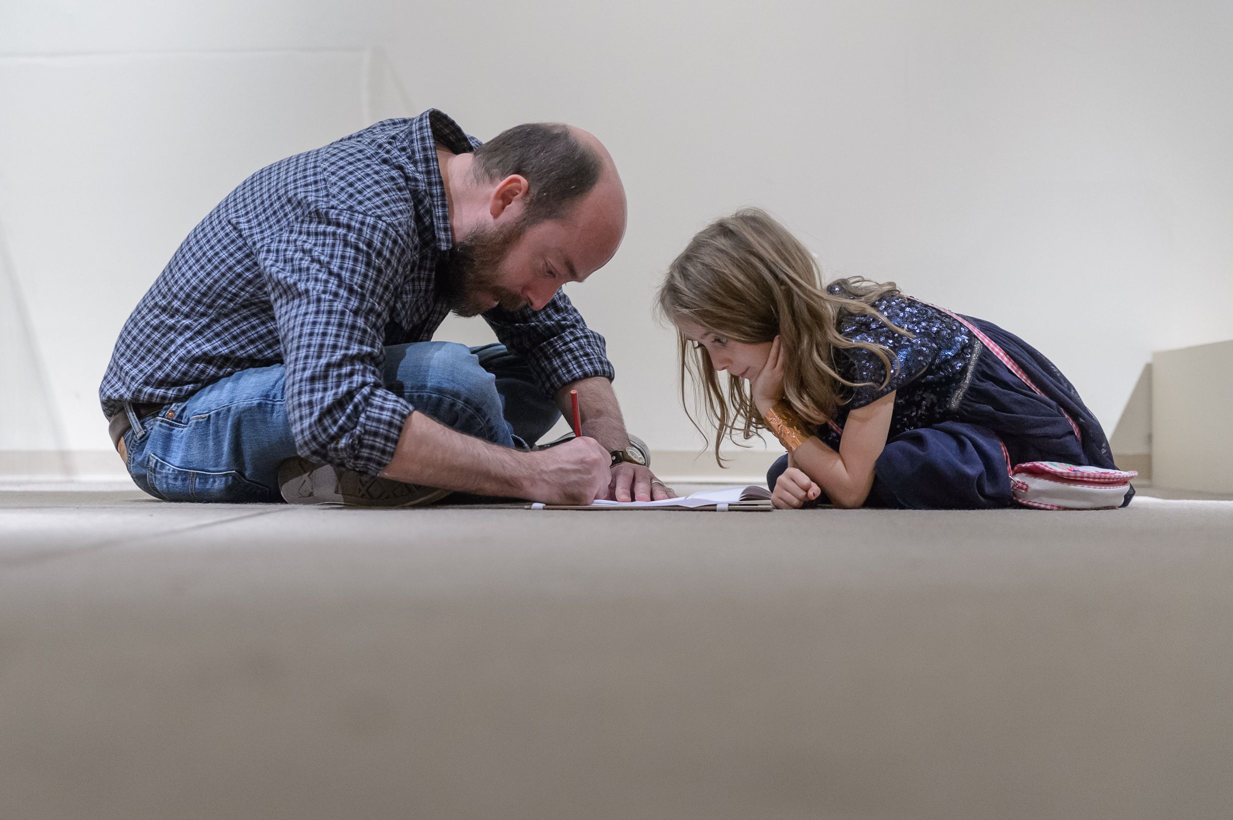 A mid-aged man and a young girl huddle together on the floor engrossed in an activity together.
