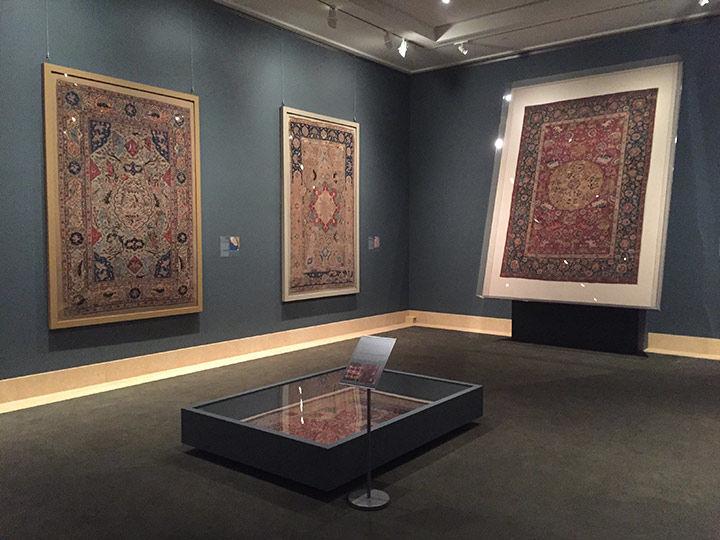 View of gallery with three Persian carpets hanging on dark blue-grey walls