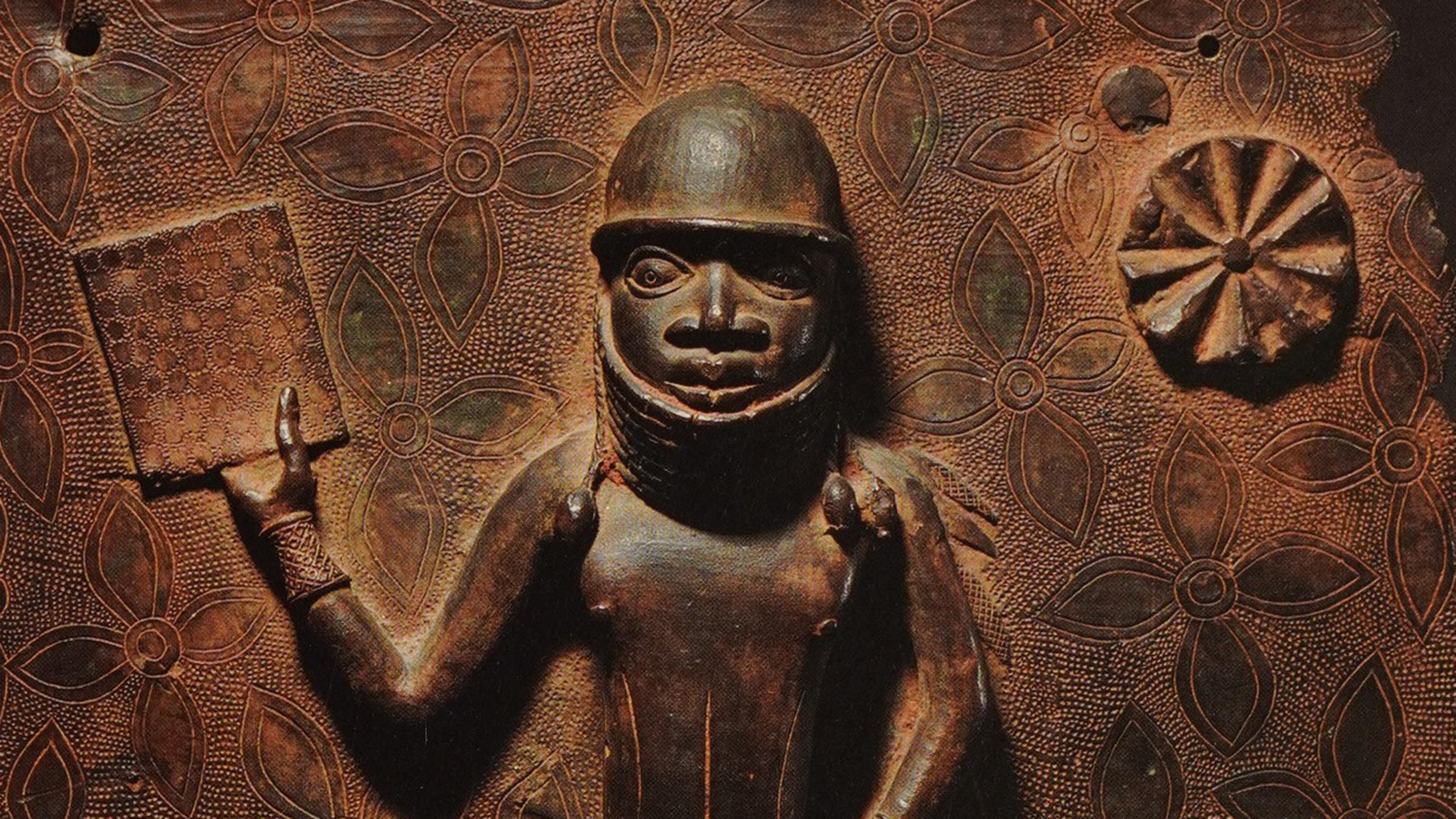 Bronze Benin sculpture with a figure holding a book. The background is adorned with floral motifs