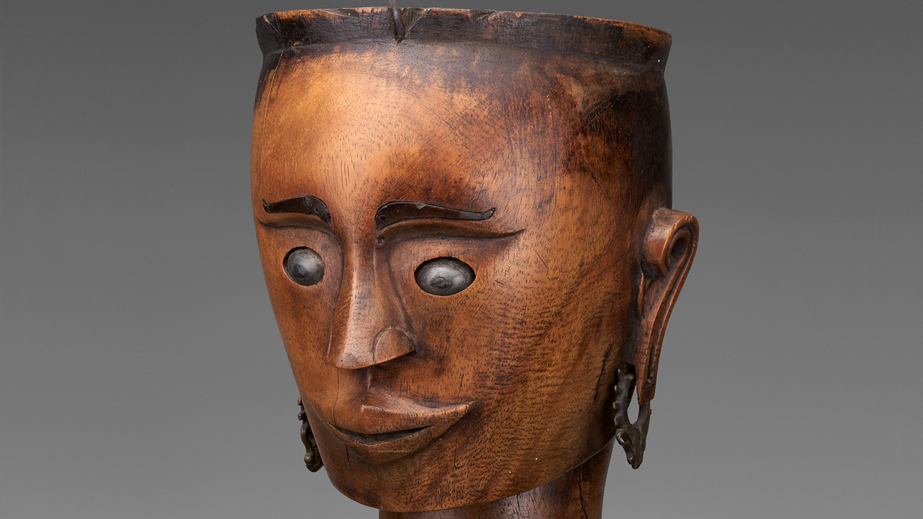 Wood puppet head with a face carved in.