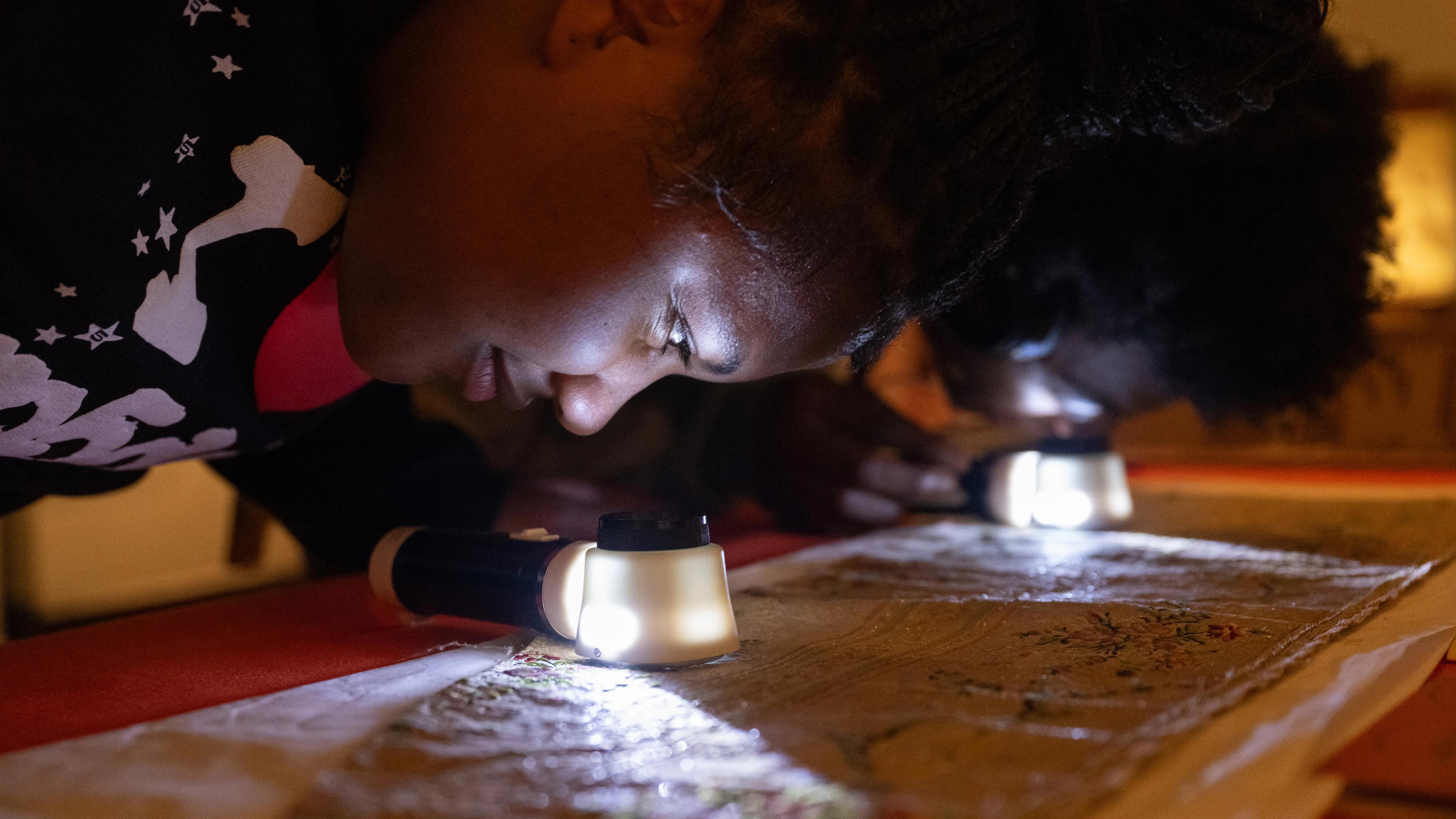 Teen looking up close at a magnifying glass with a light to examine an artwork more closely.