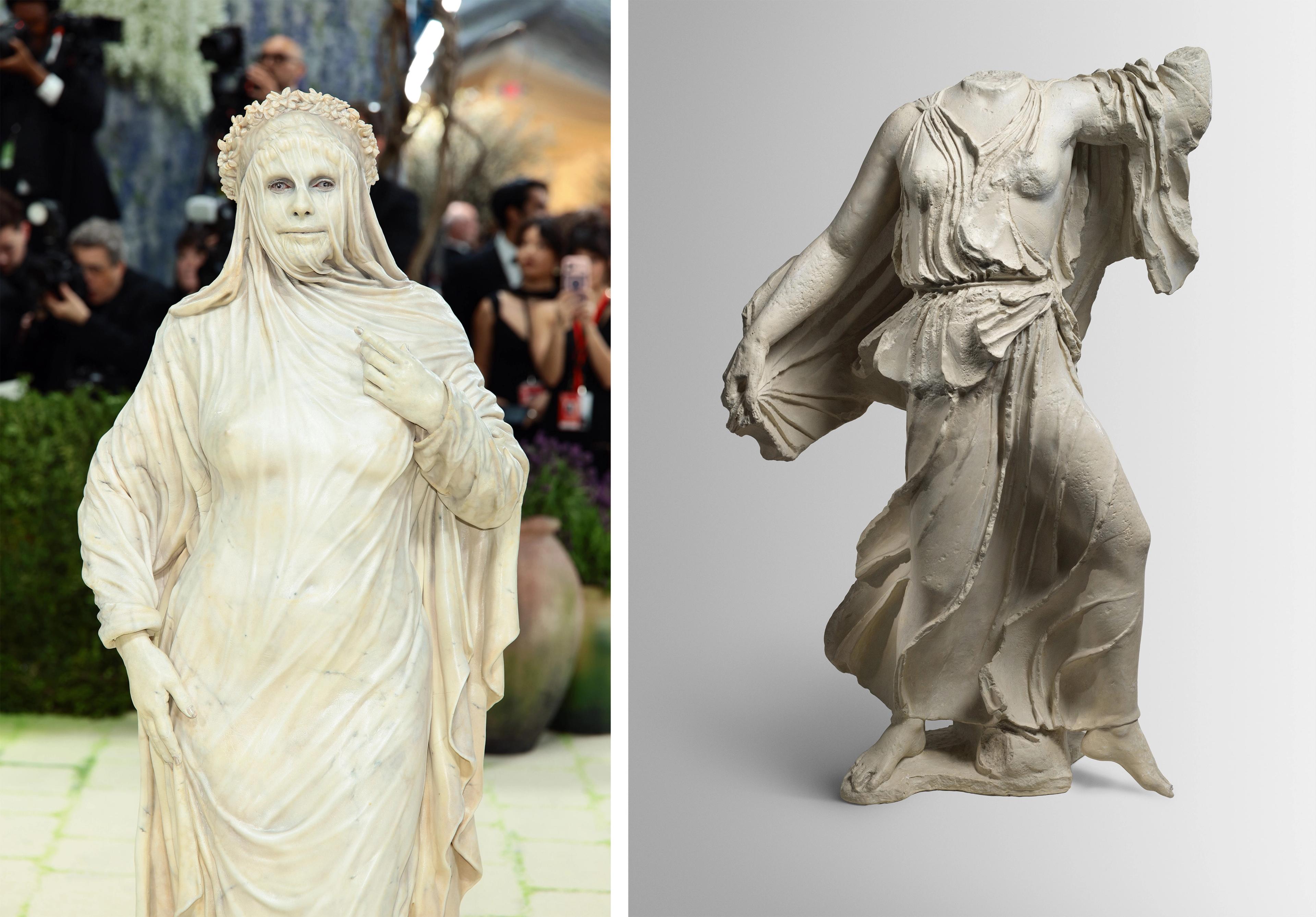 A person dressed in a white marble-like gown, resembling a Greek statue, stands confidently on a green carpet. Next to them is a headless ancient statue.